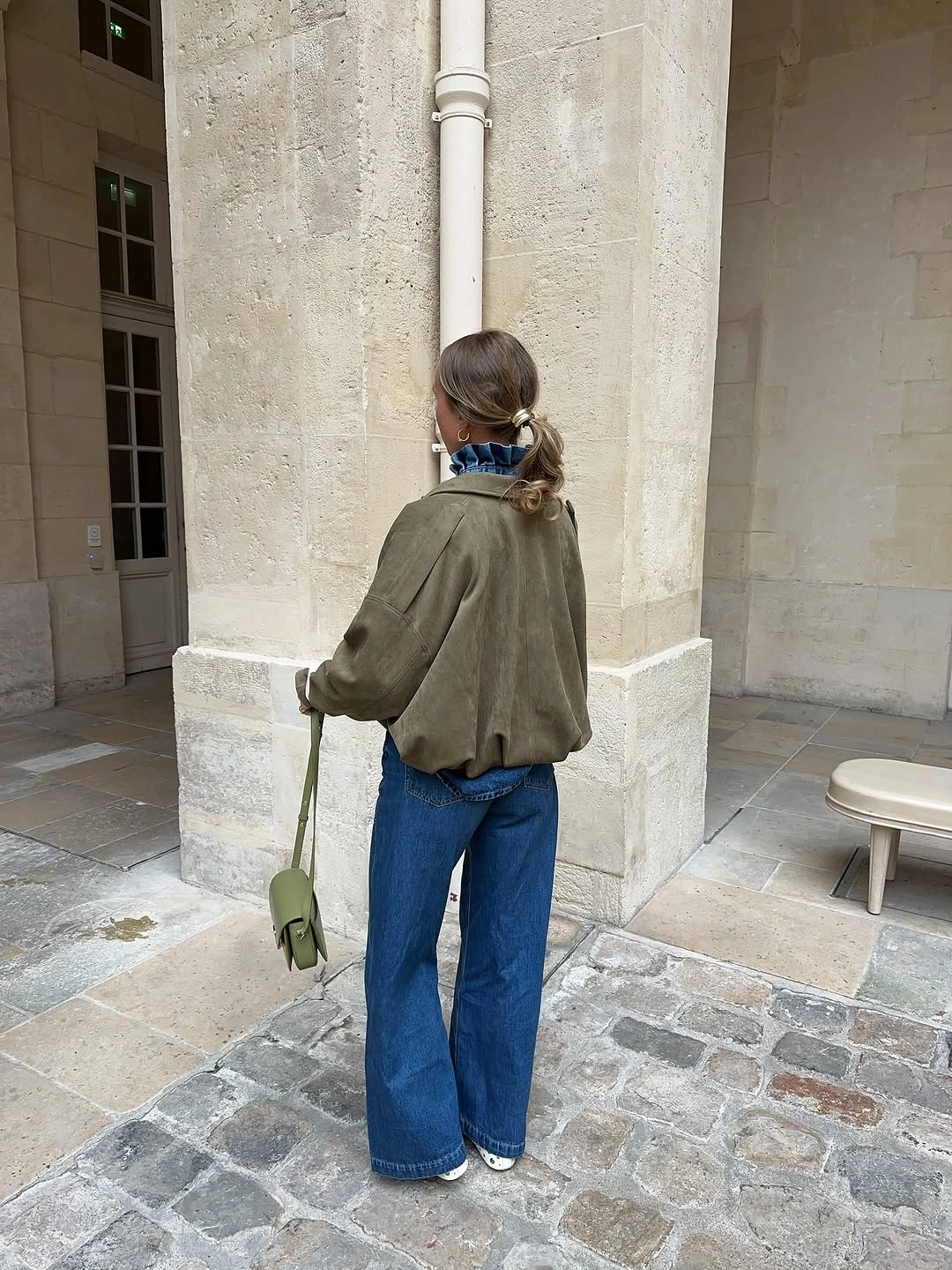 Olive cropped jacket, blue jeans, pale green bag, and light shoes