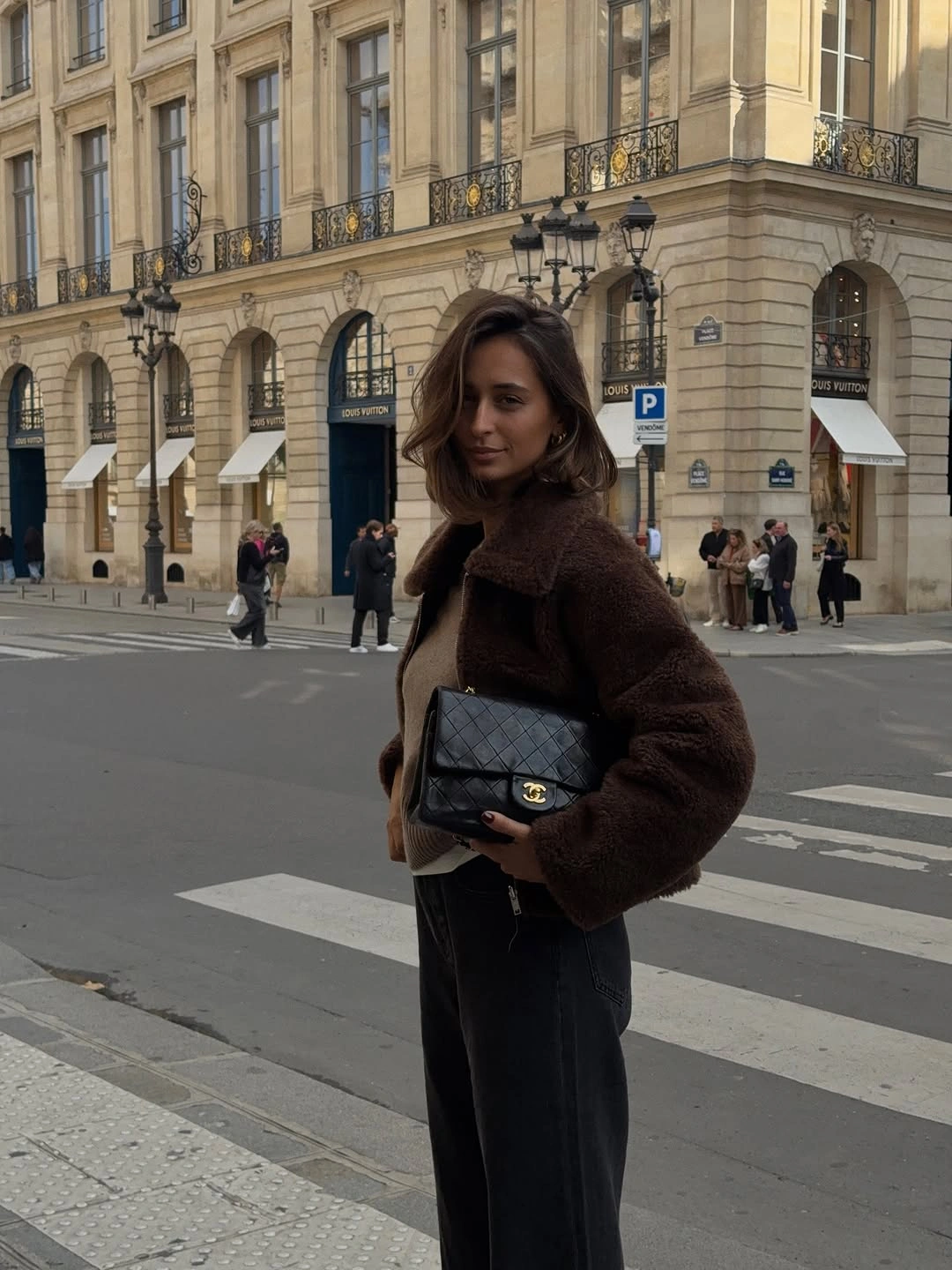 Brown teddy-looking jacket, taupe top, dark trousers, and quilted-looking chain bag