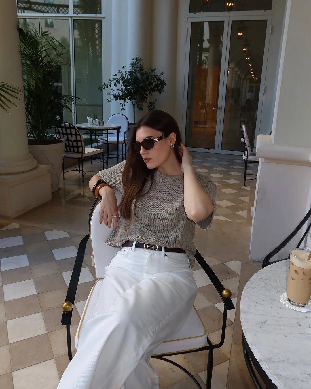 Taupe sweater, white trousers, dark belt, sunglasses, and small accessories