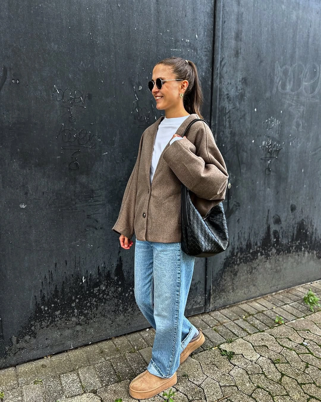 Taupe buttoned layer, white top, blue jeans, and black tote