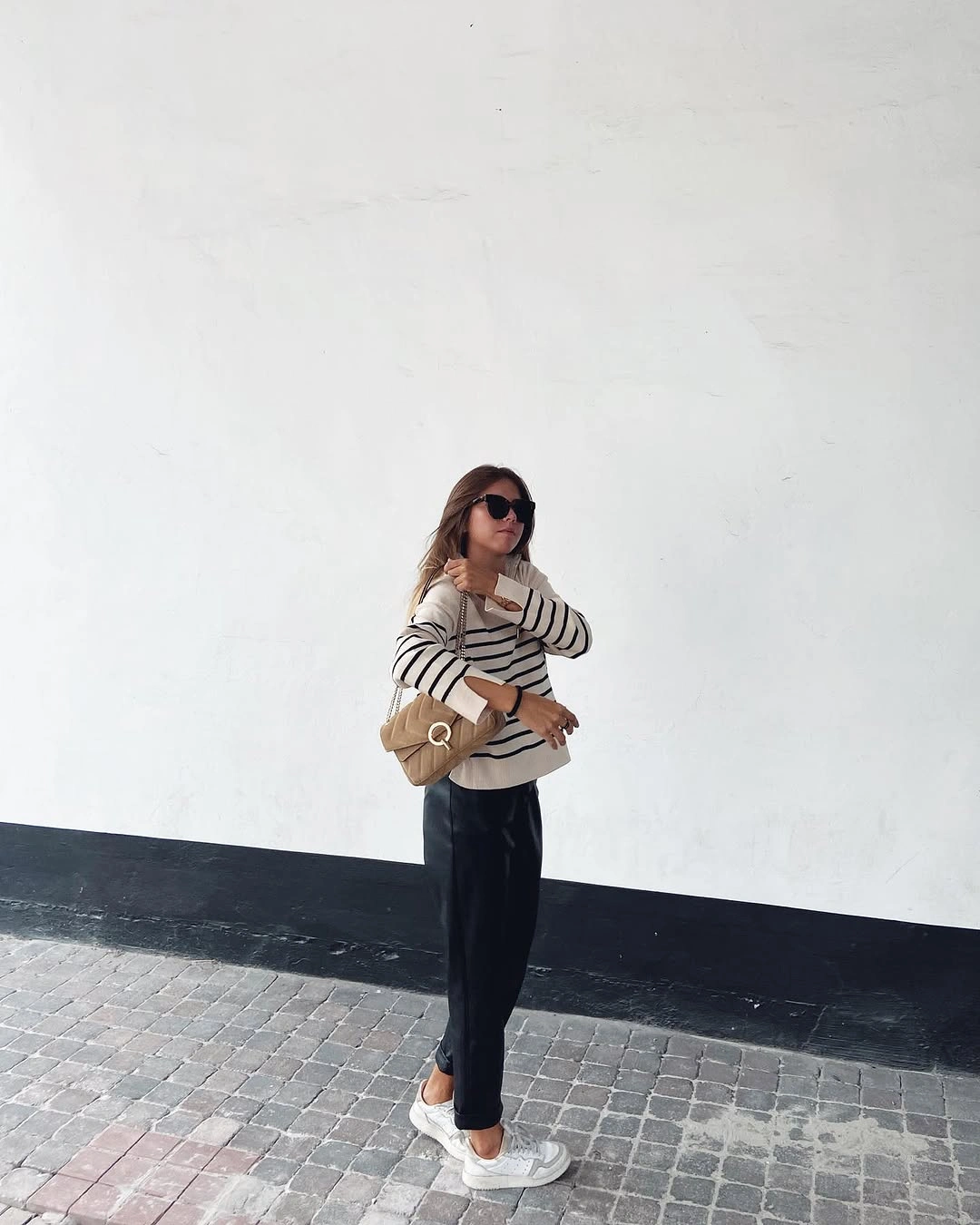 Striped sweater, black trousers, beige crossbody bag, and white sneakers