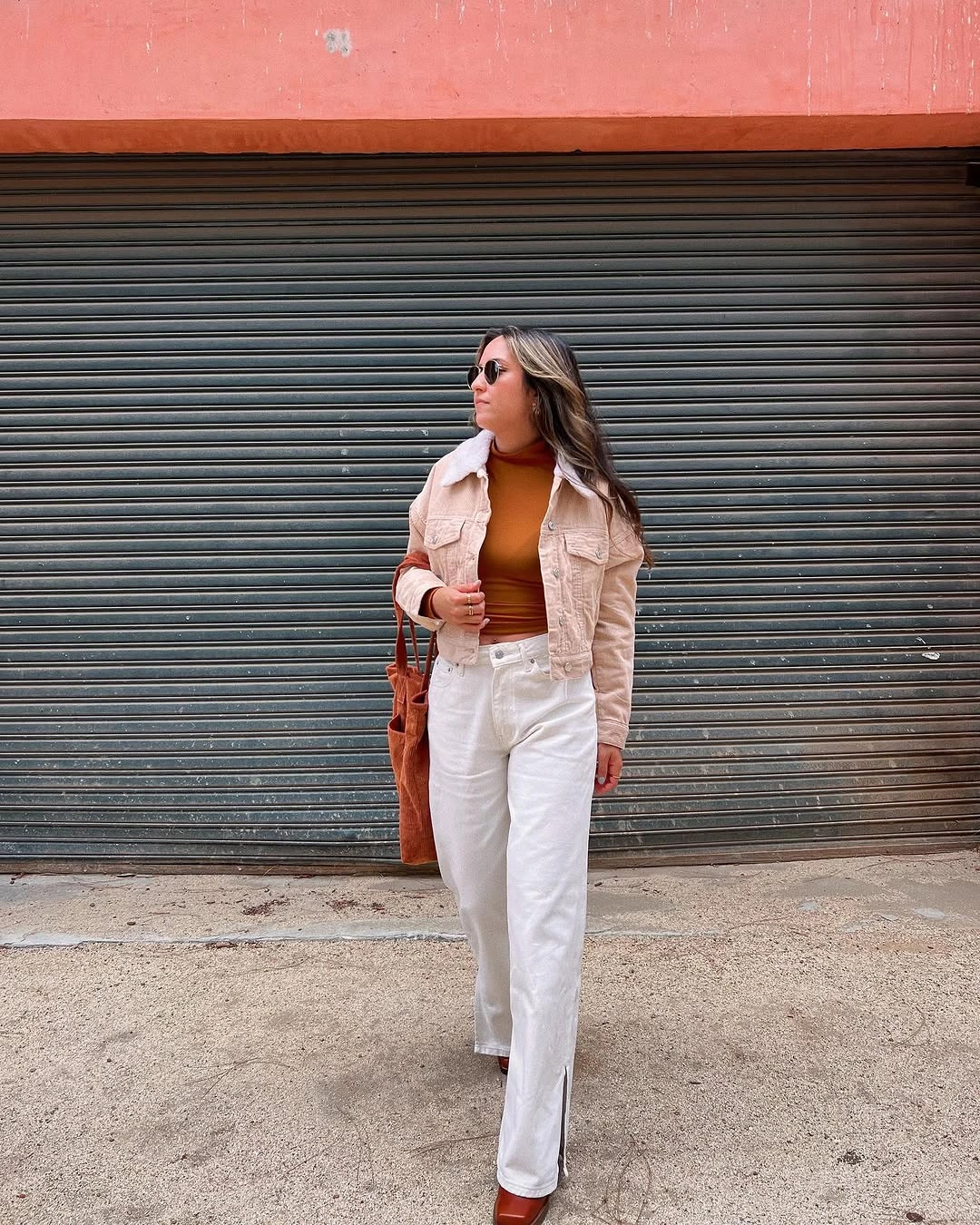 Cream jacket, orange-brown top, white trousers, brown bag, and brown shoes