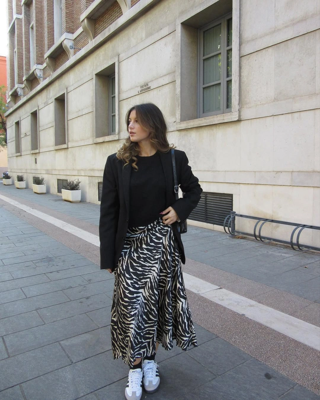 Black top, zebra-like long skirt, sneakers, and dark shoulder bag