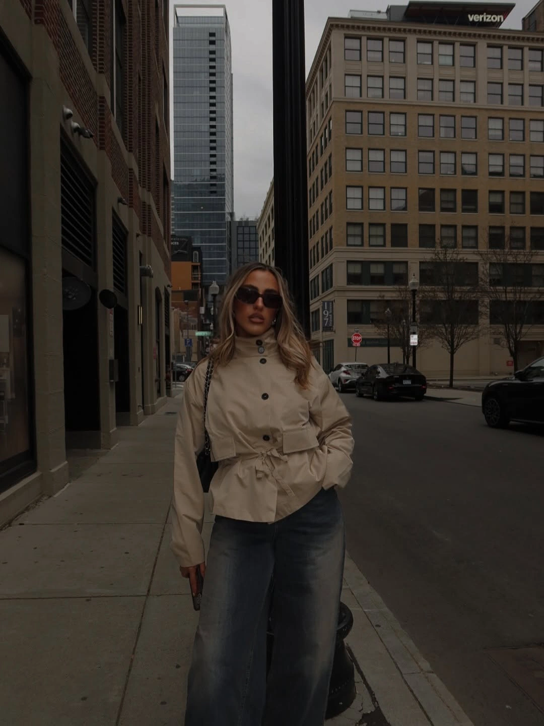 Beige belted light jacket with wide blue jeans and sunglasses