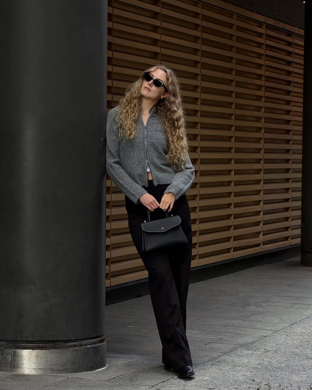 Gray zip-front knit-looking top with black trousers and black handbag