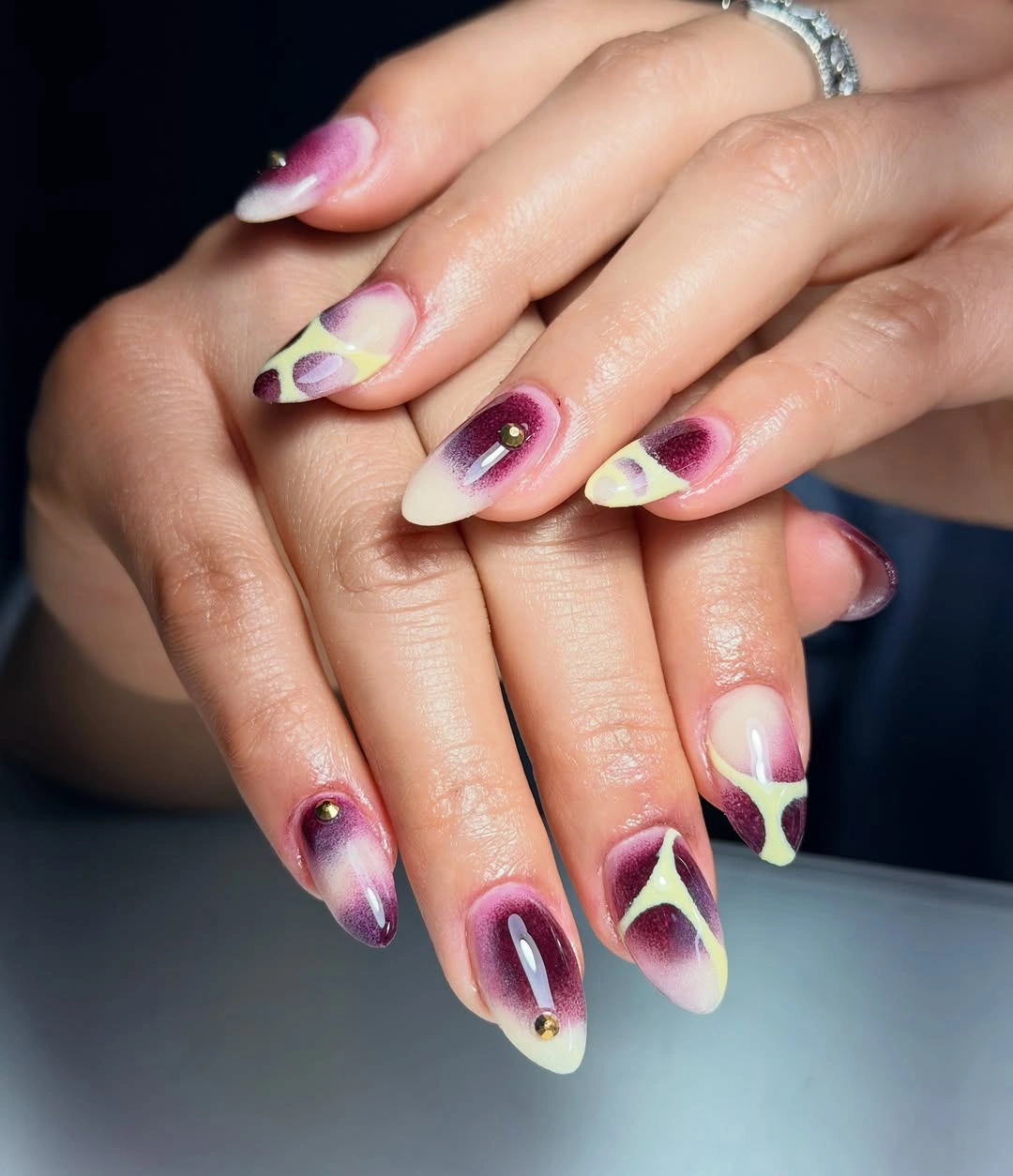 Pink-purple nails with pale yellow-green petal-like motifs and dots