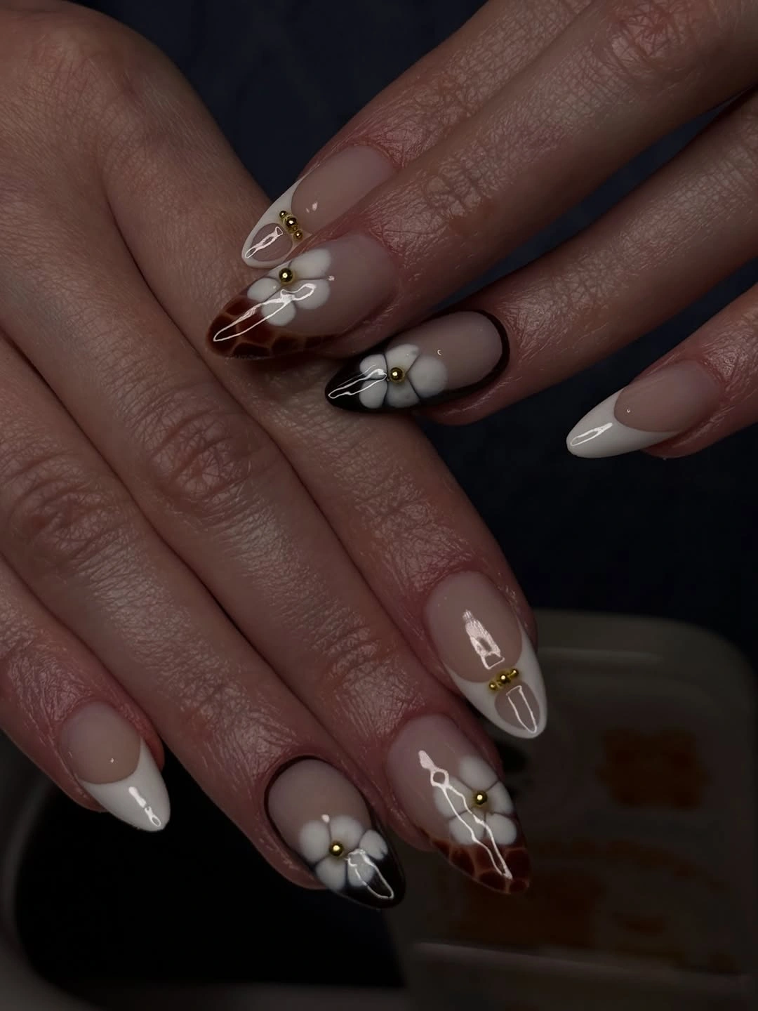 Nude almond nails with brown marbled areas and white flower-like accents