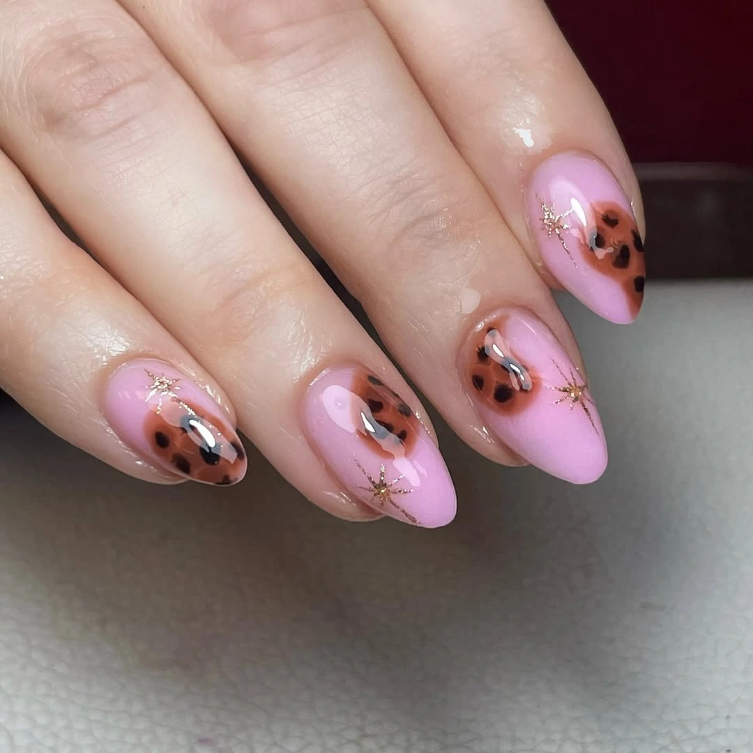 Pink almond nails with brown leopard-like patches and gold starbursts