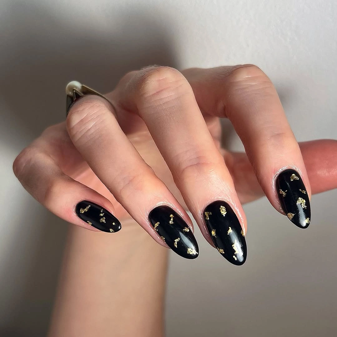 Black almond nails scattered with irregular gold-colored flecks