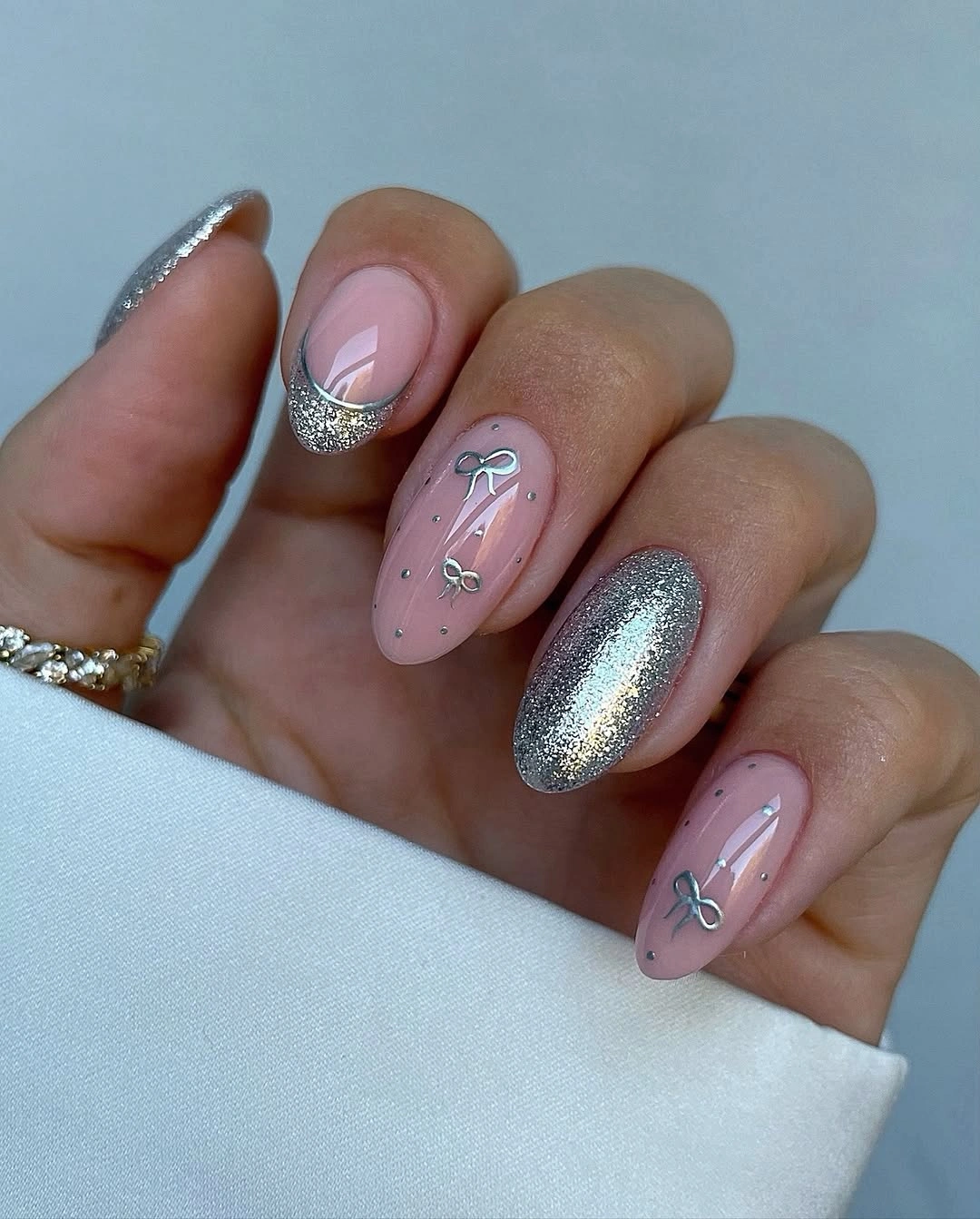 Soft pink almond nails with silver bows dots and glittering tips