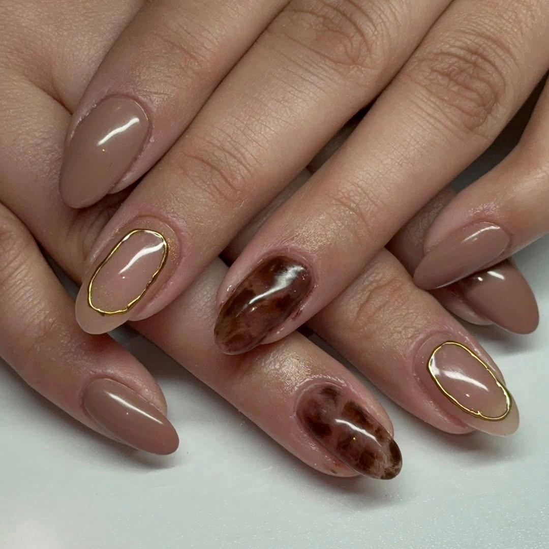 Taupe almond nails with brown marbled accents and gold-colored oval outlines