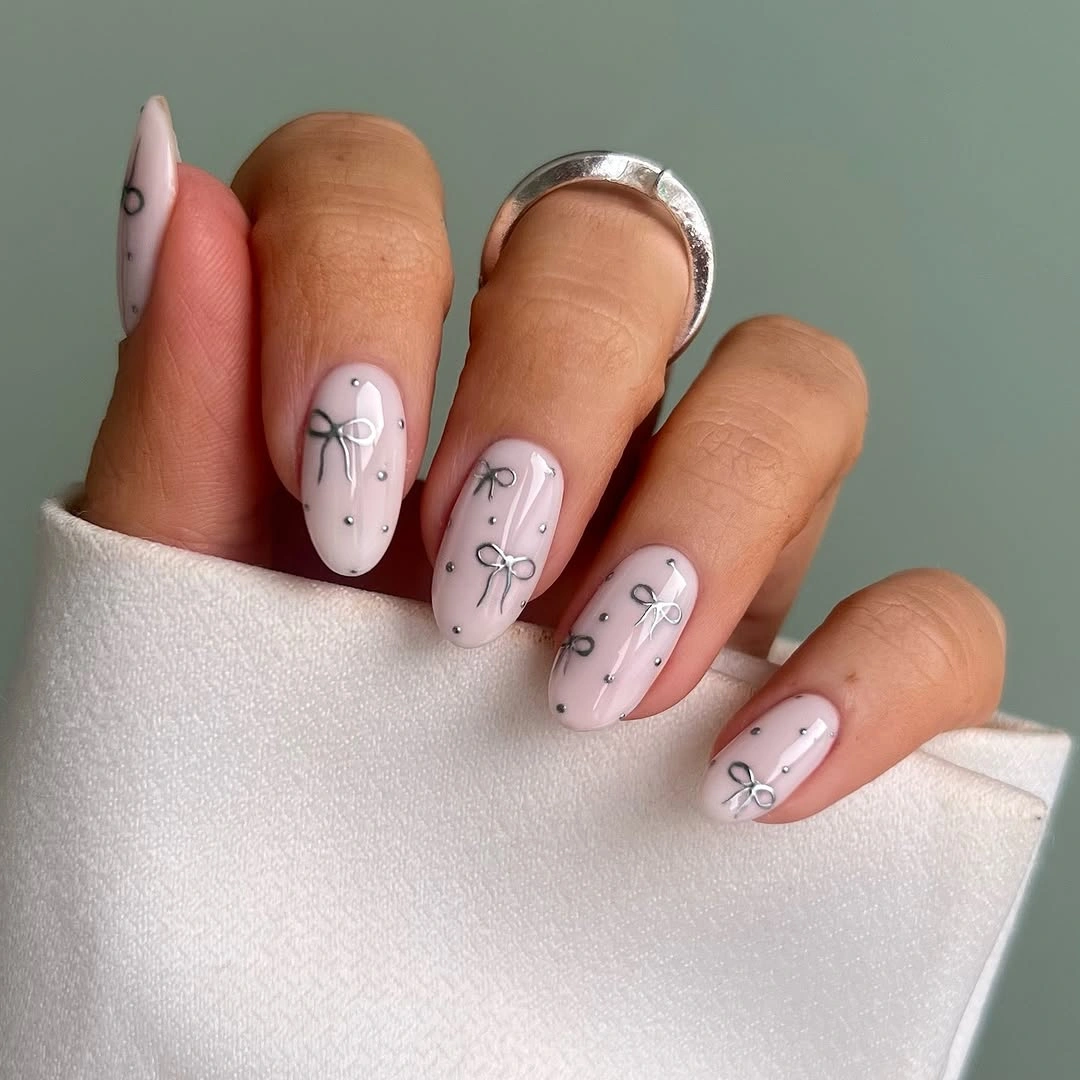 Pale pink almond nails with silver bows and dot accents