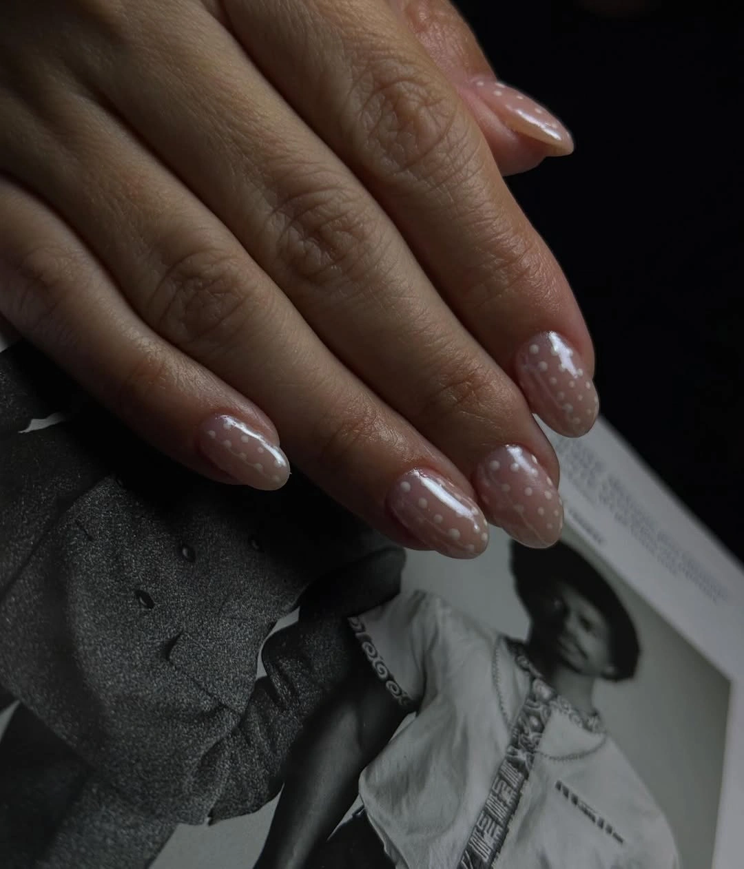 Oval blush-pink nails with scattered white dots and curved strokes