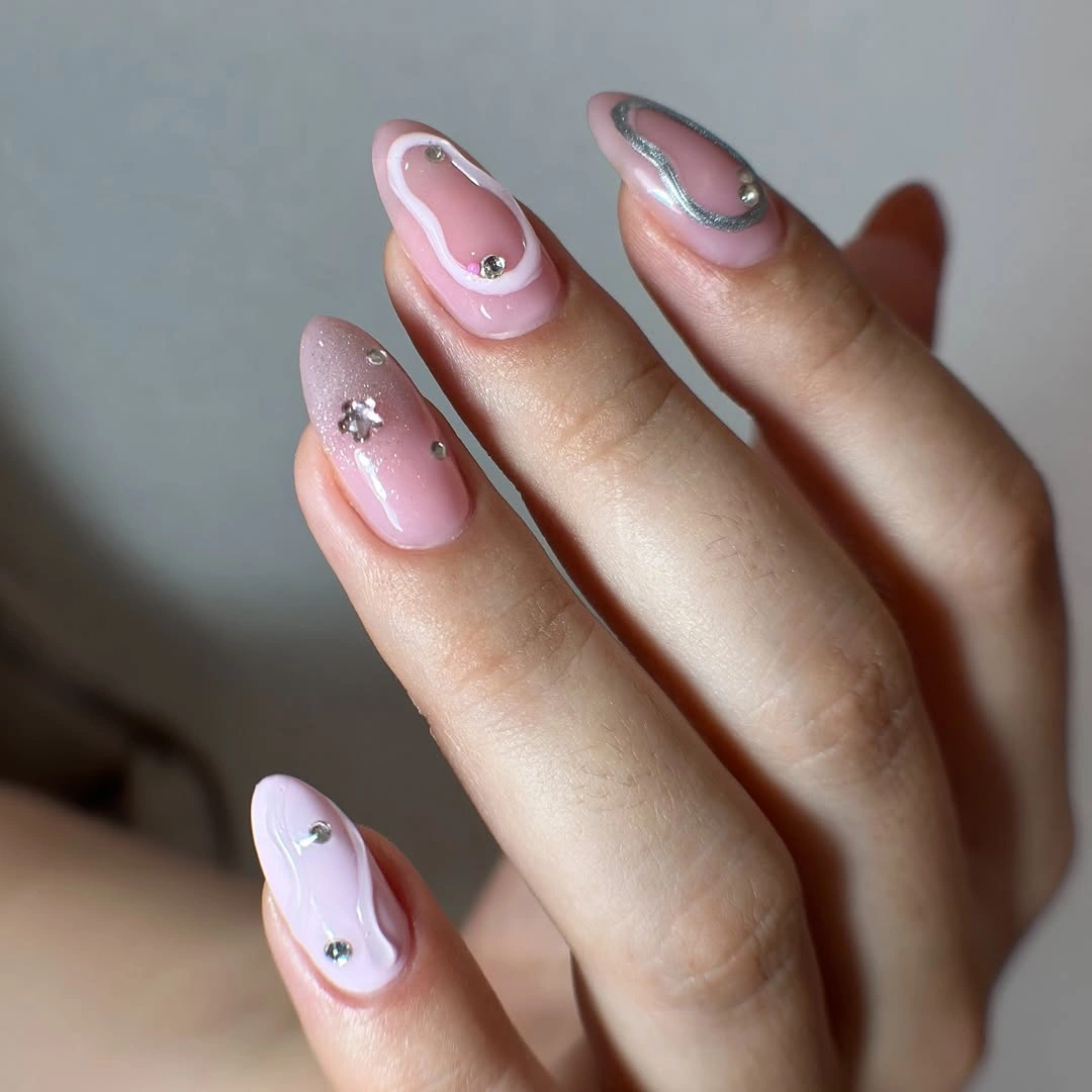 Blush almond nails with silver curves and tiny gem-like accents