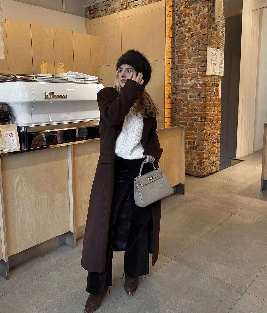 Long brown coat, white sweater, dark pants, gray handbag