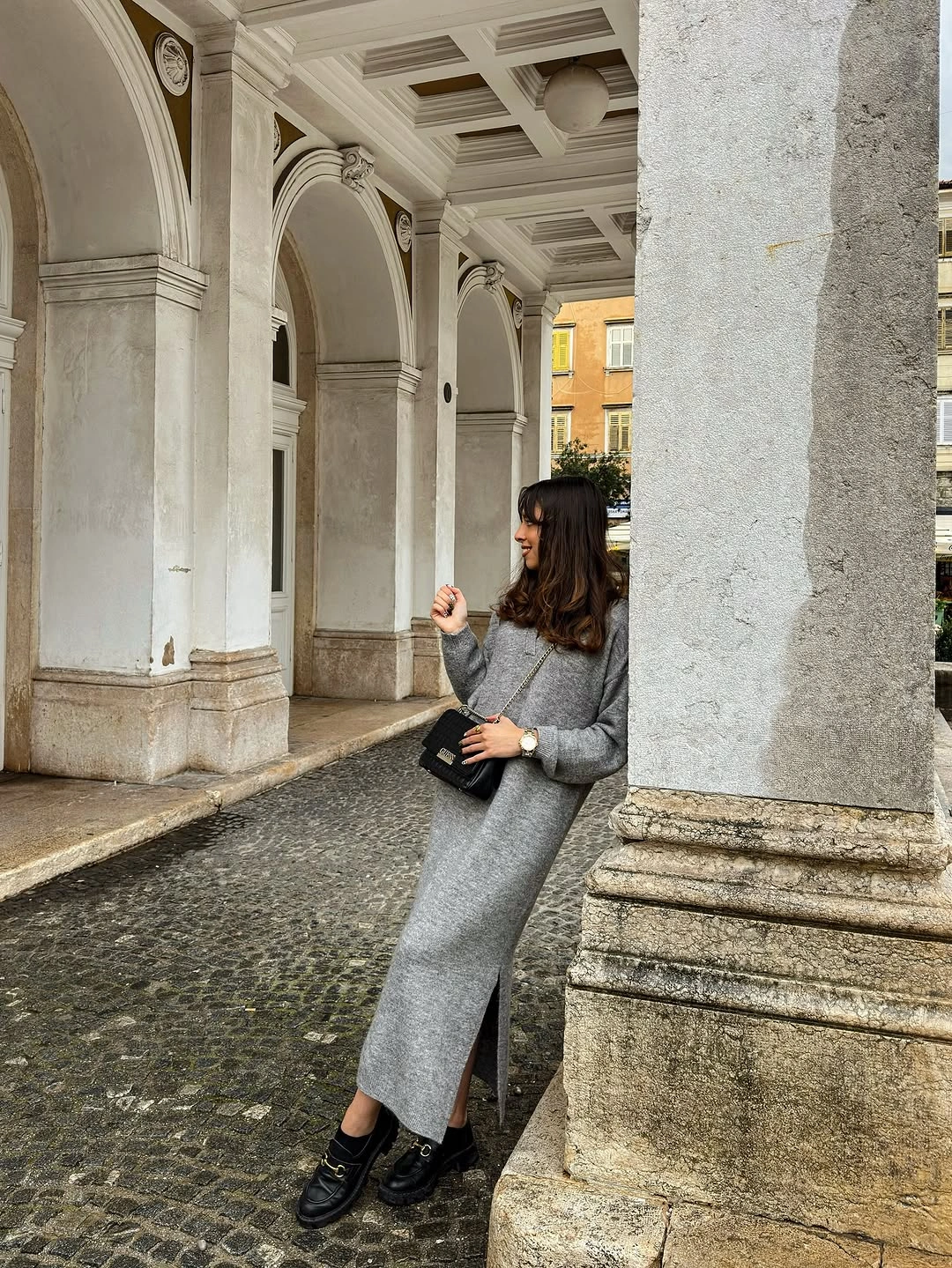 Long gray outfit, black shoes, black bag, stone arches