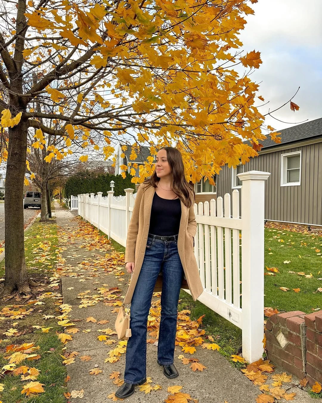 Tan long layer, black top, blue jeans, pale shoulder bag