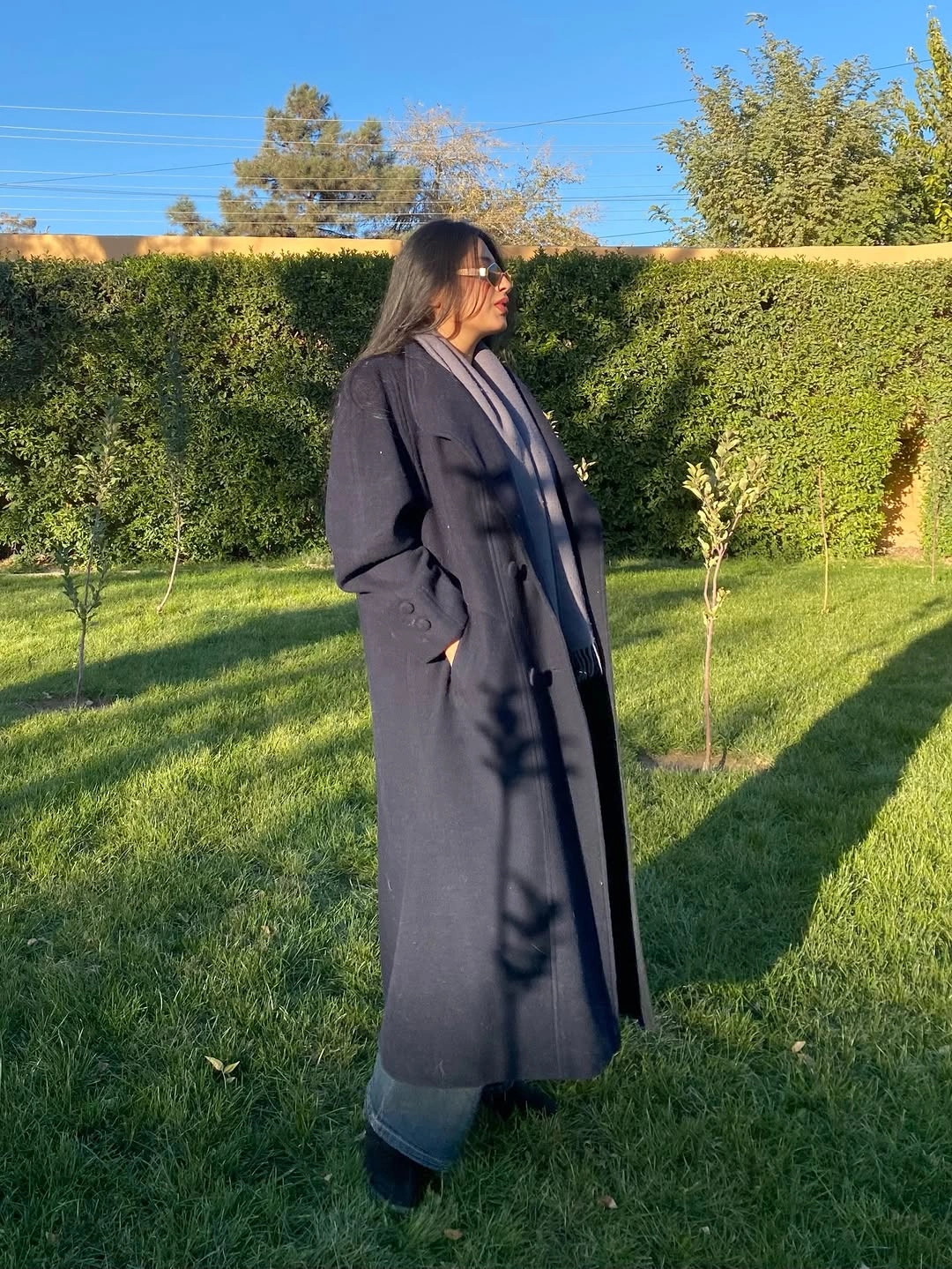 Long dark coat, gray scarf, blue jeans, dark shoes