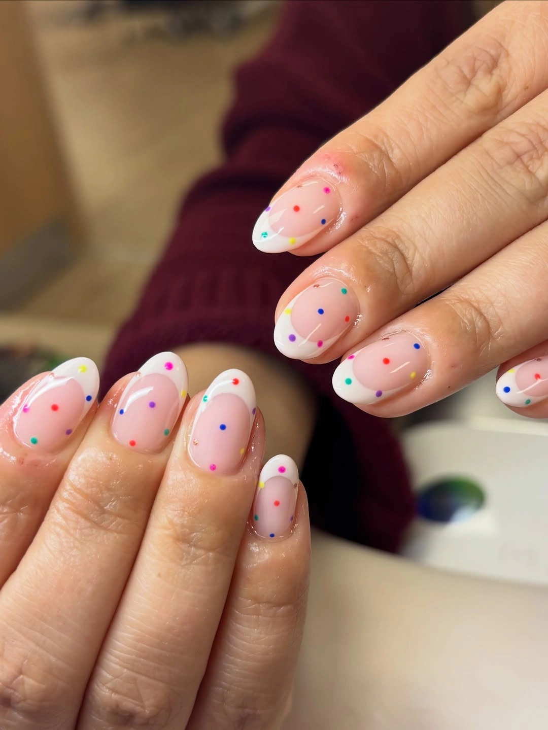 Light almond French-inspired nails with neon accents and multicolor polka dots