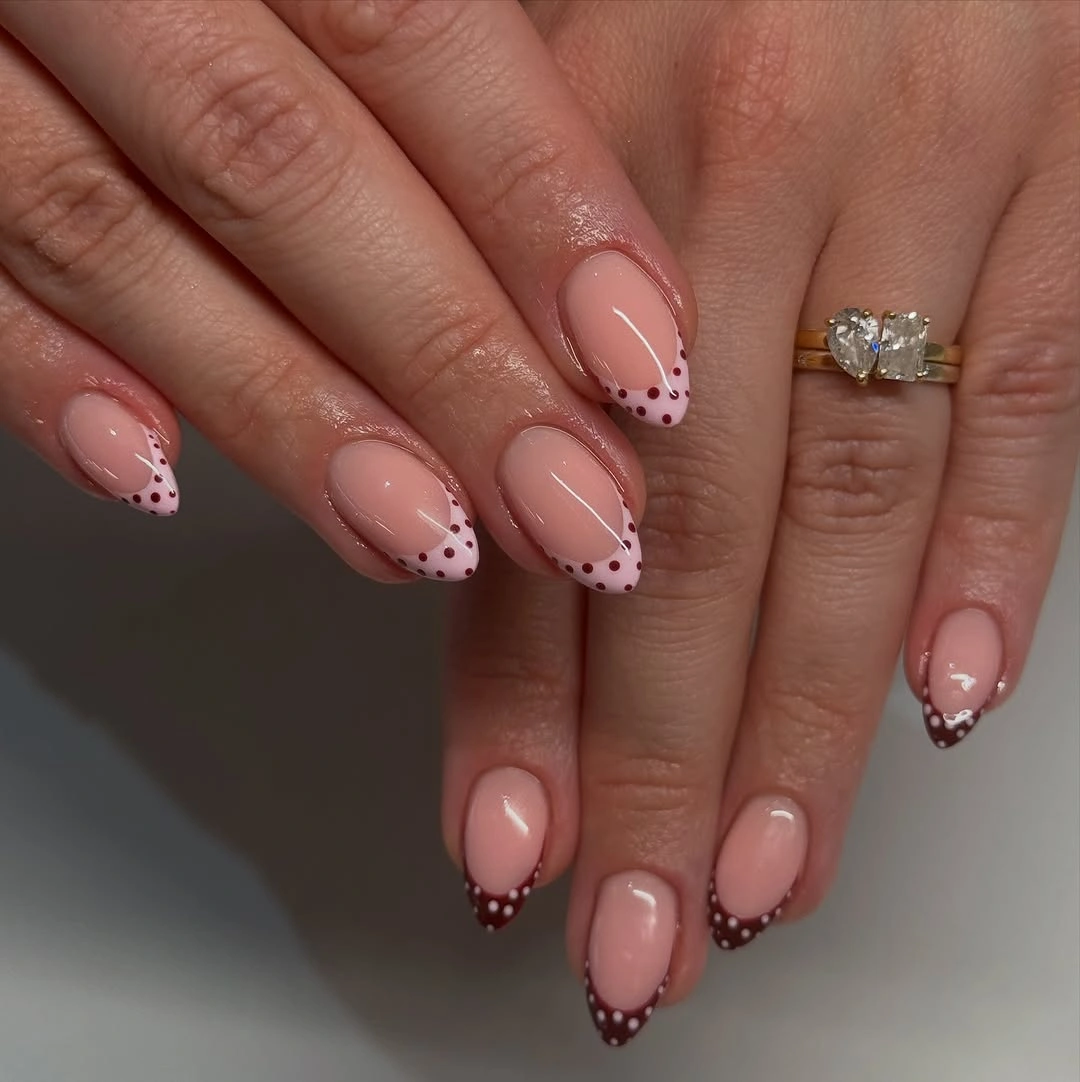 Soft nude almond nails with fine dotted dark edges and delicate black curves