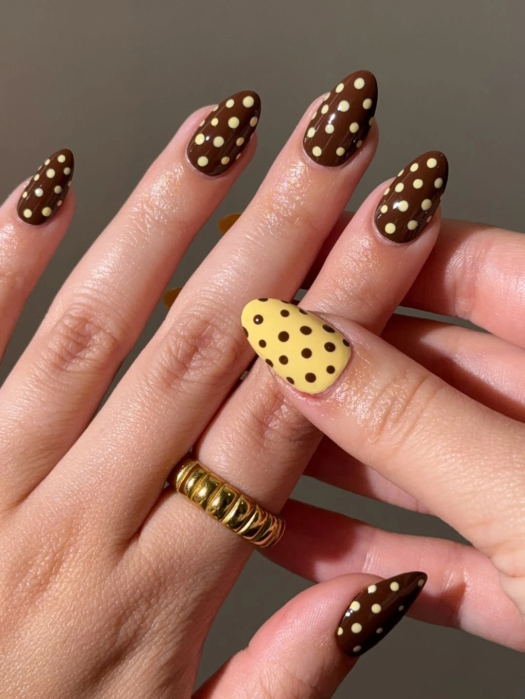 Chocolate brown almond nails with cream polka dots and one yellow accent nail