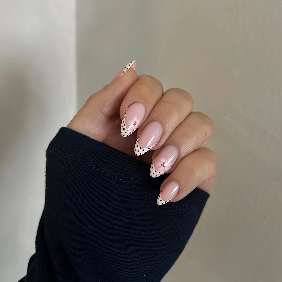 Soft nude almond nails with white French tips and tiny black polka dots
