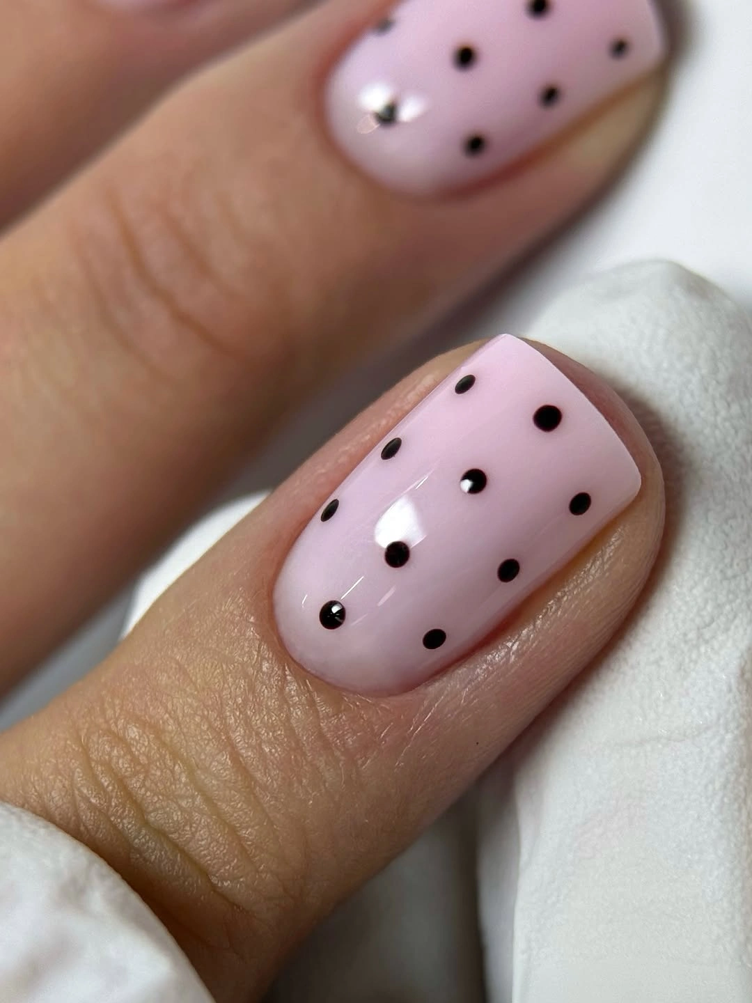 Soft pink rounded nails with spaced black polka dots and tiny accents