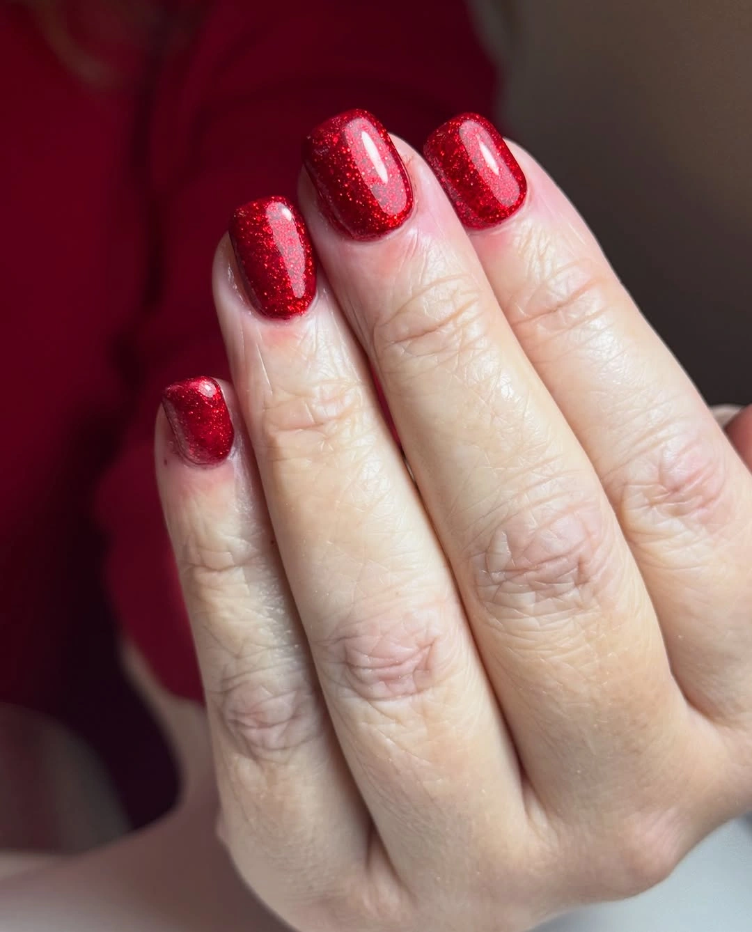Short rounded nails covered in uniform sparkling red