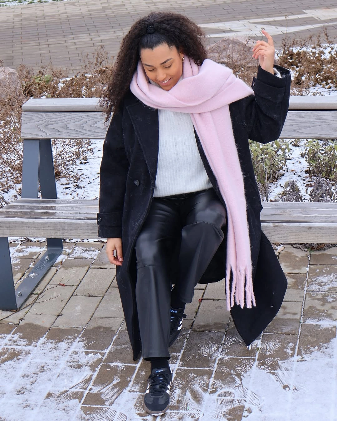 Black coat with oversized pink scarf, white knit, dark pants, and loafers