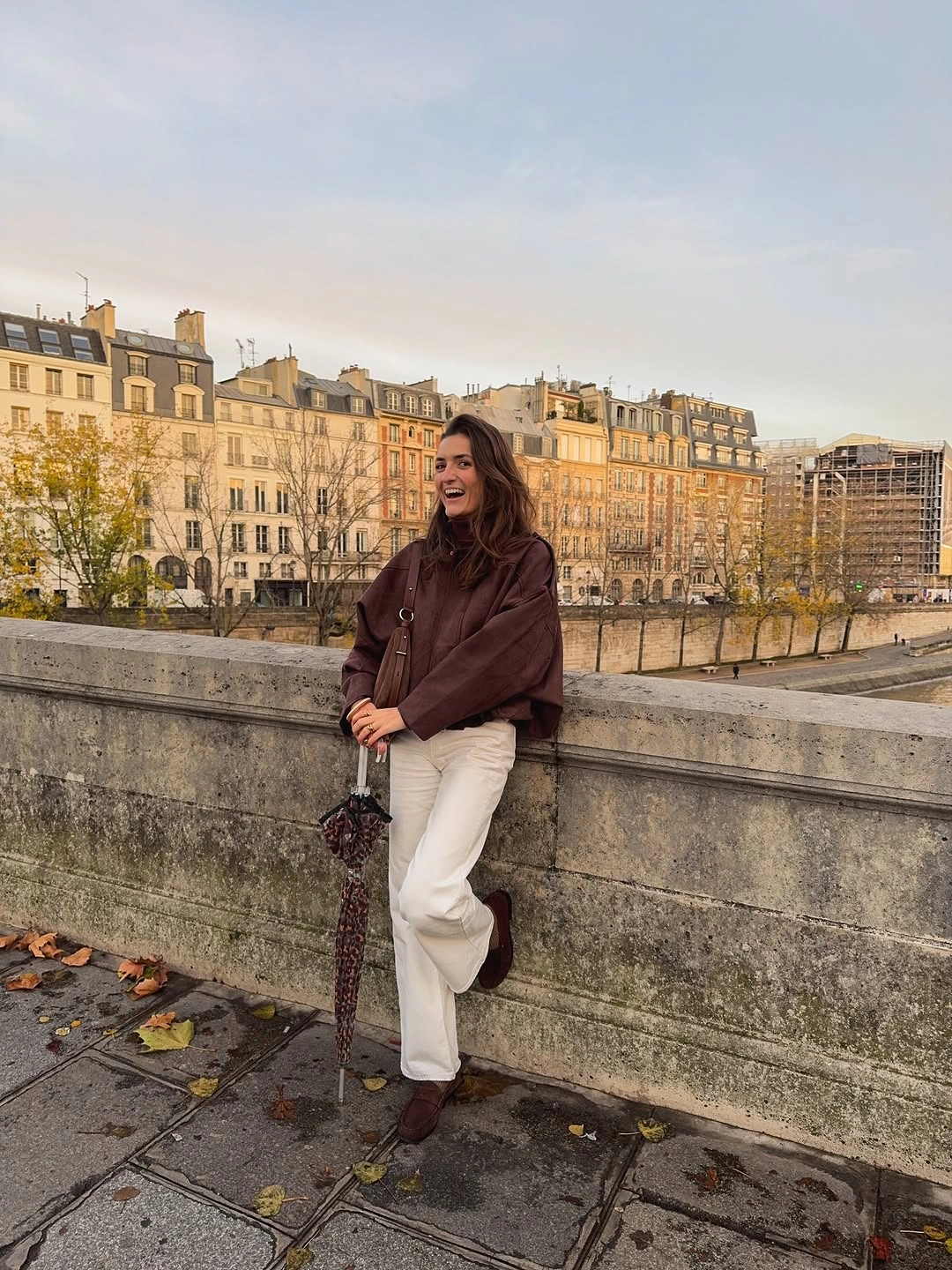 Short brown jacket with white wide pants, brown boots, and small brown bag