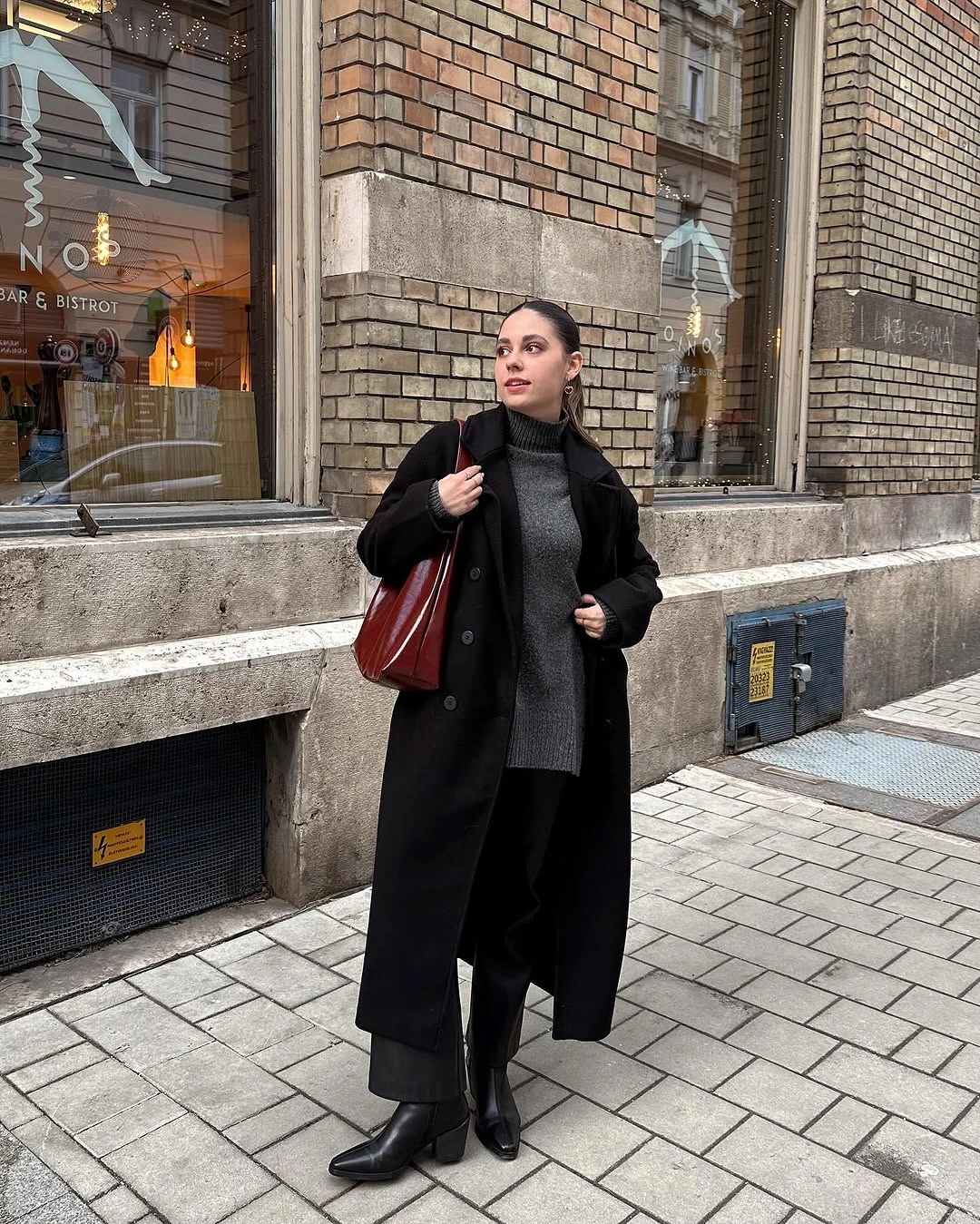 Long black coat with black scarf, black boots, and burgundy shoulder bag