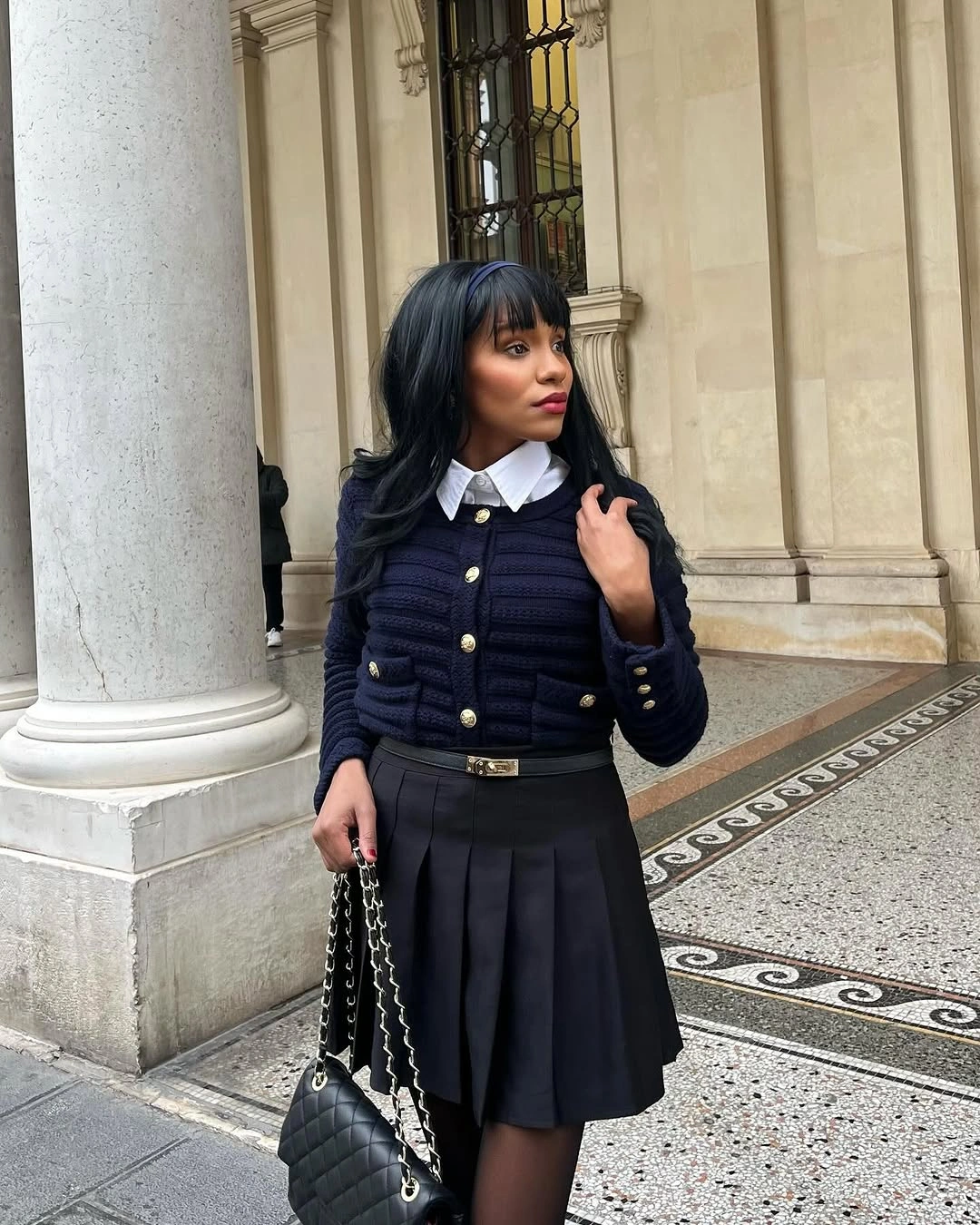 Navy cardigan with white shirt collar, pleated skirt, black tights, and handbag