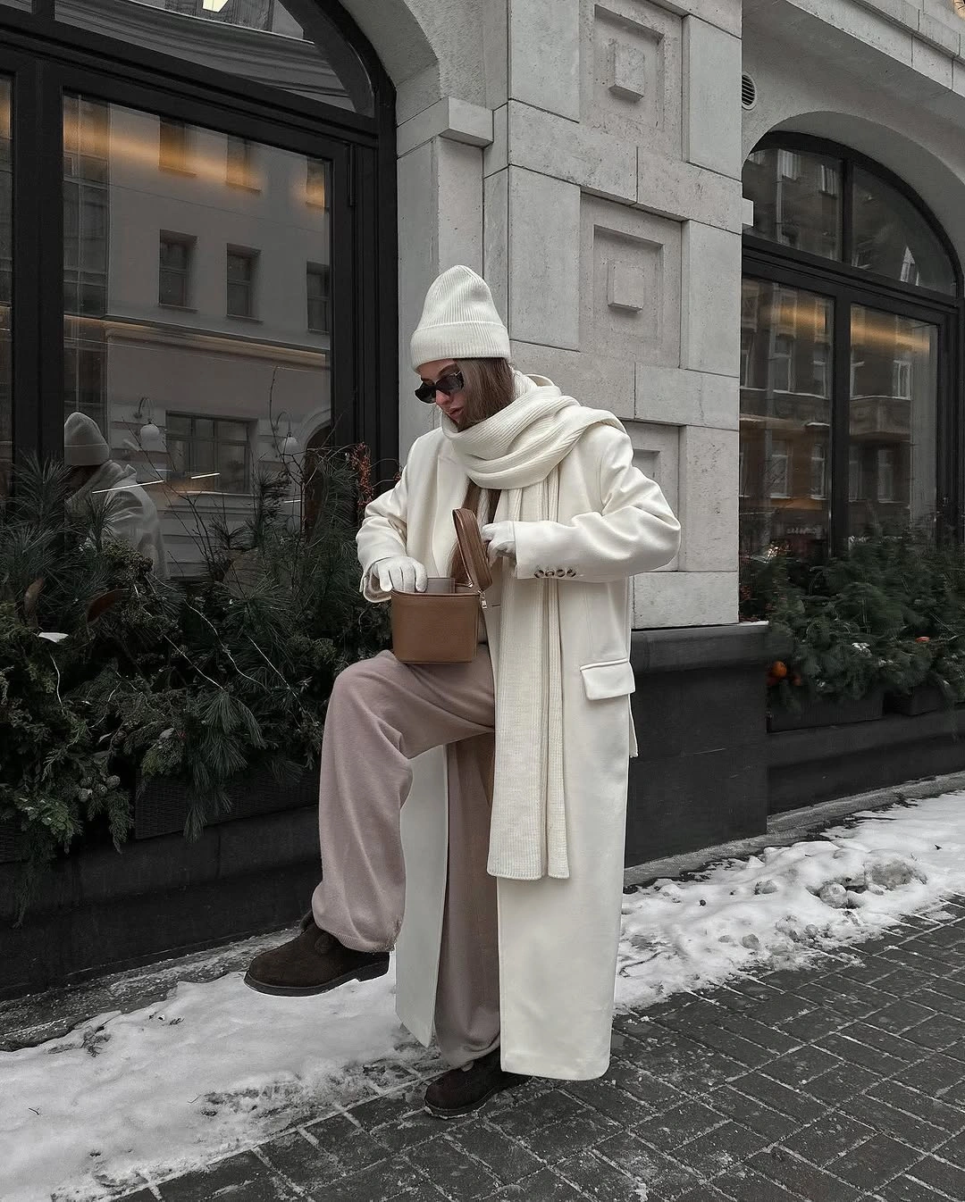 Long ivory wrap coat with pale wide trousers, beige bag, and black boots