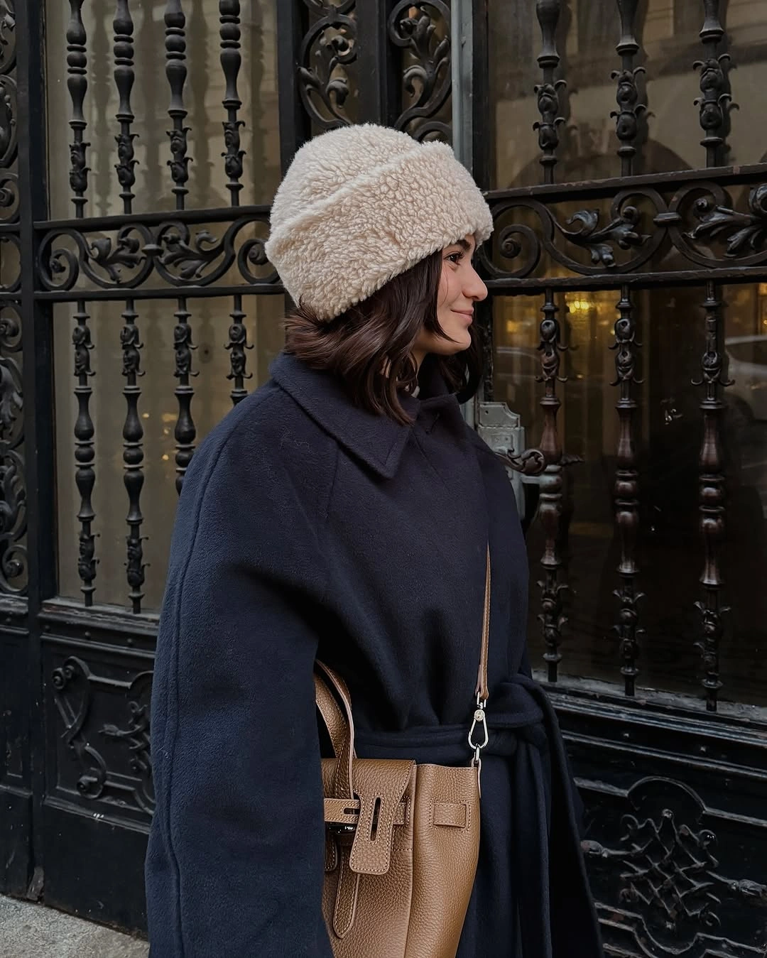 Navy cape-style coat with cream textured bucket hat and tan crossbody bag