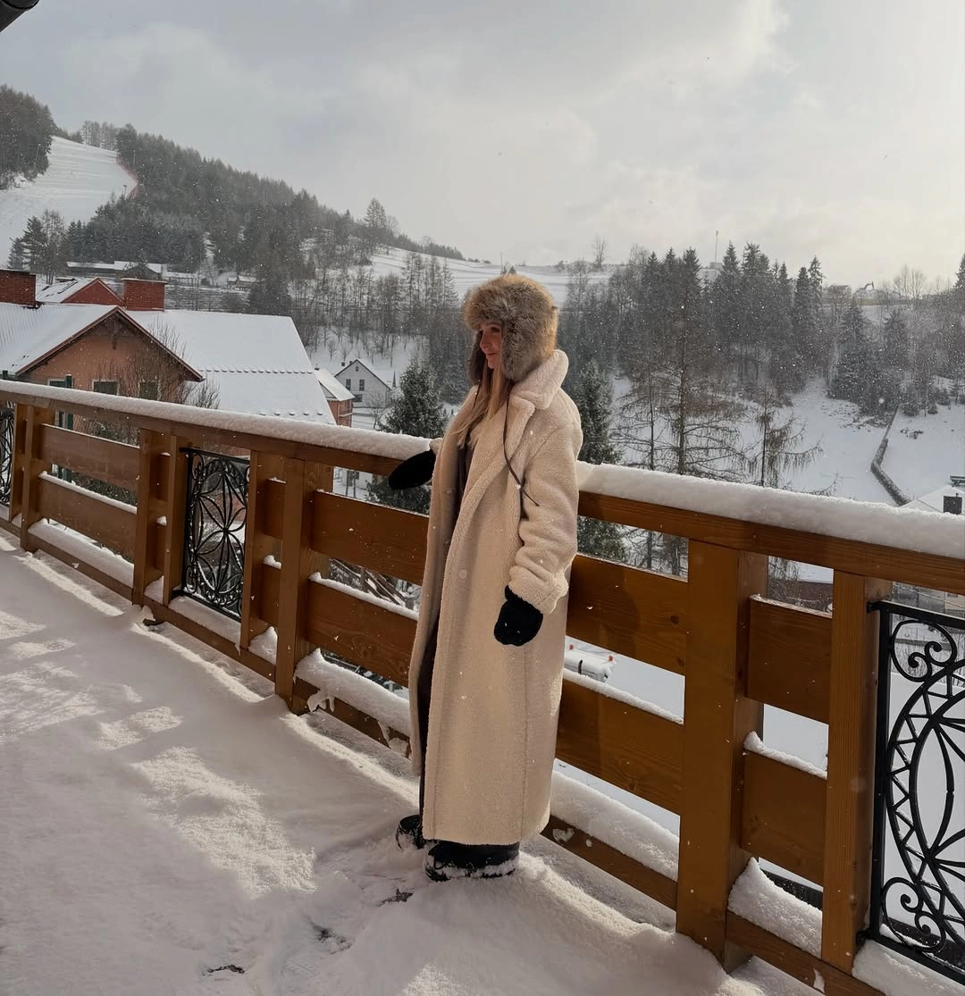 Long cream teddy-style coat with brown textured hat and dark pants