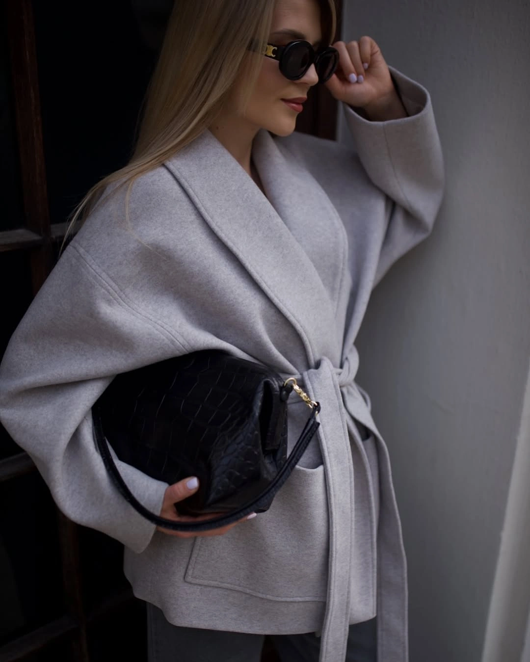 Light gray belted coat with sunglasses and black handbag