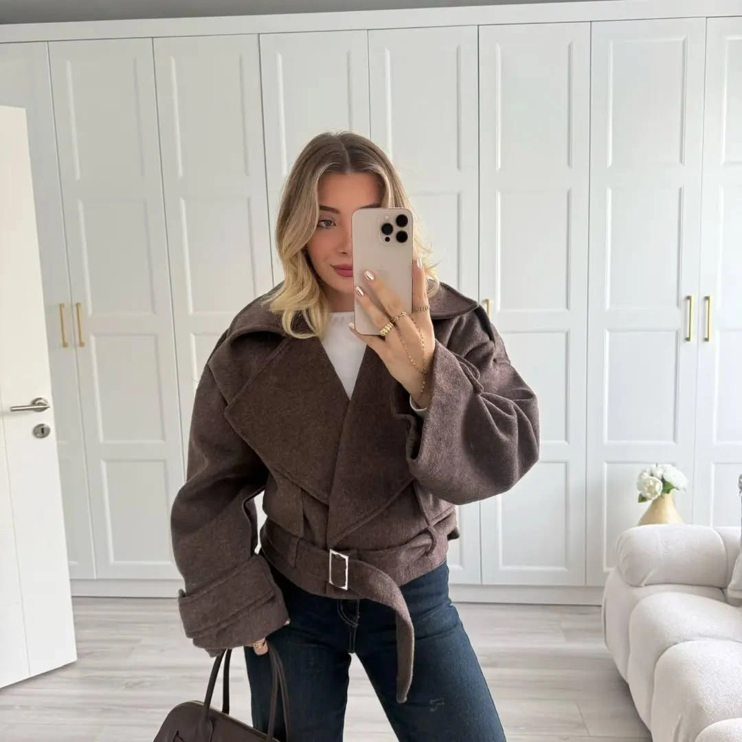 Taupe short coat with belt, dark jeans, and handbag