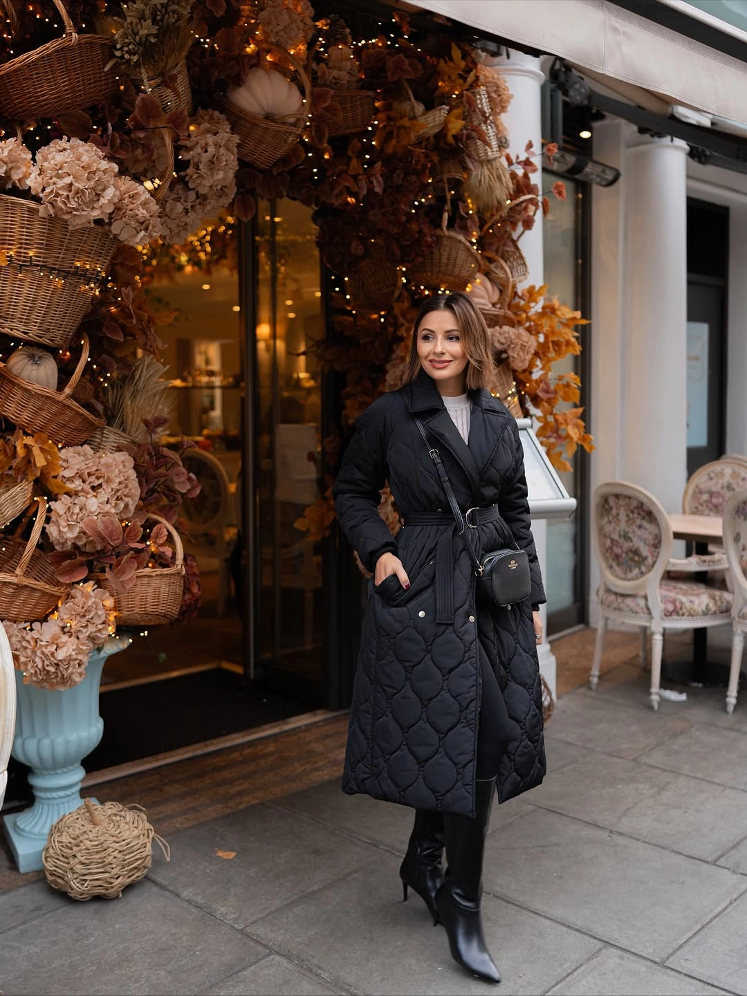 Black belted quilted coat with gray turtleneck and crossbody bag