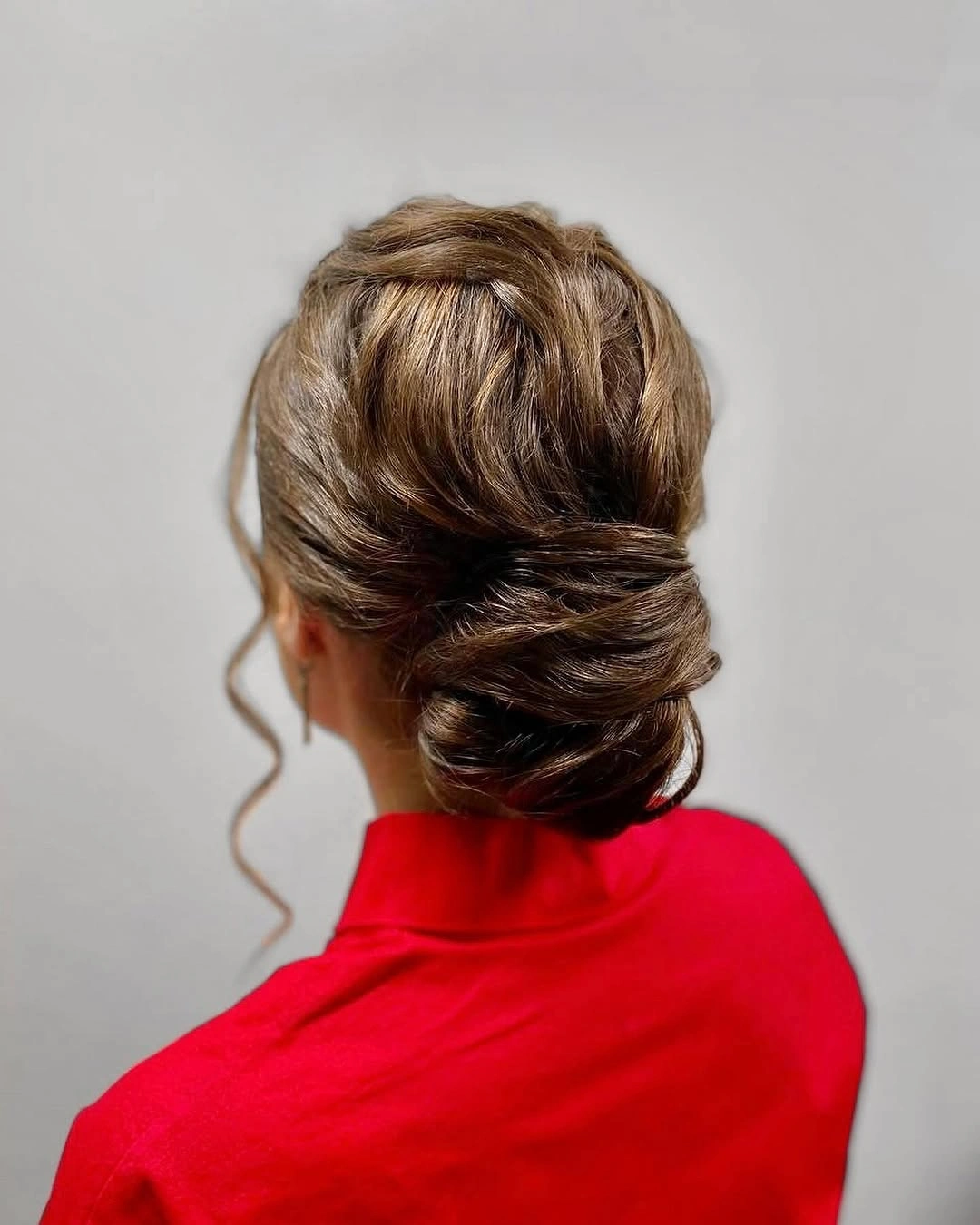 Brown low updo with smooth wrapping and loose curled strand