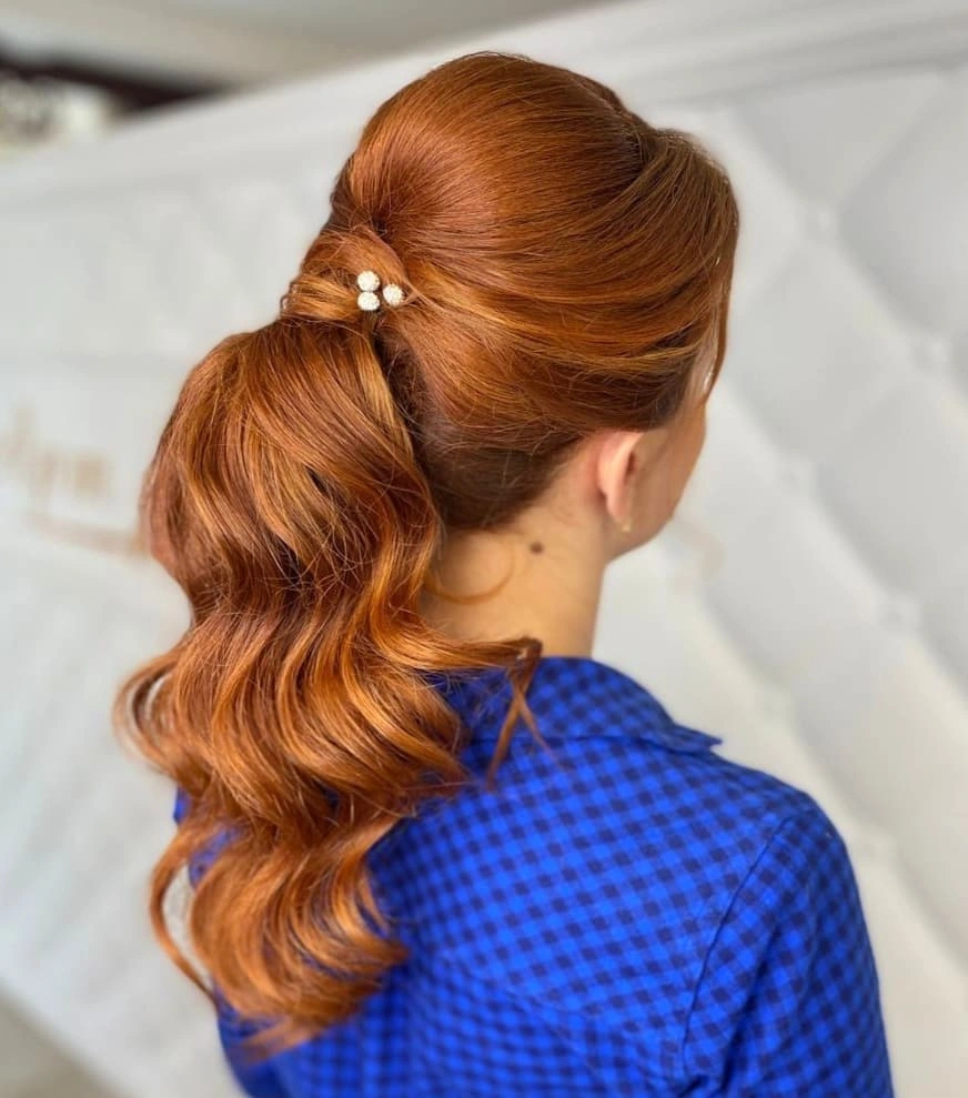 Copper-red ponytail with rounded crown, broad waves, and pearl-like accent