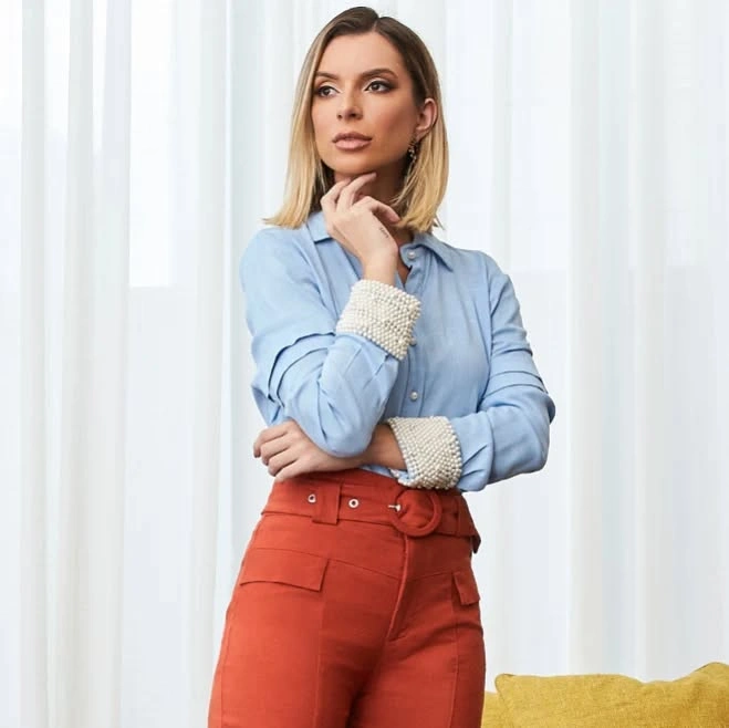 Woman in white shirt, dark pleated pants, and black straps