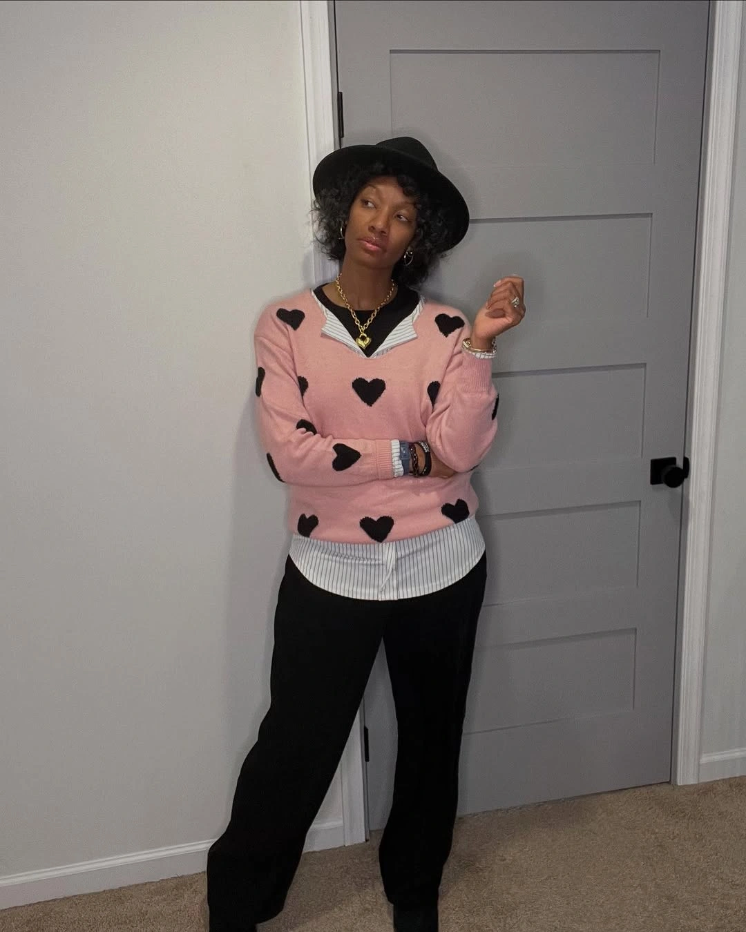 Pink heart sweater over striped shirt with black hat