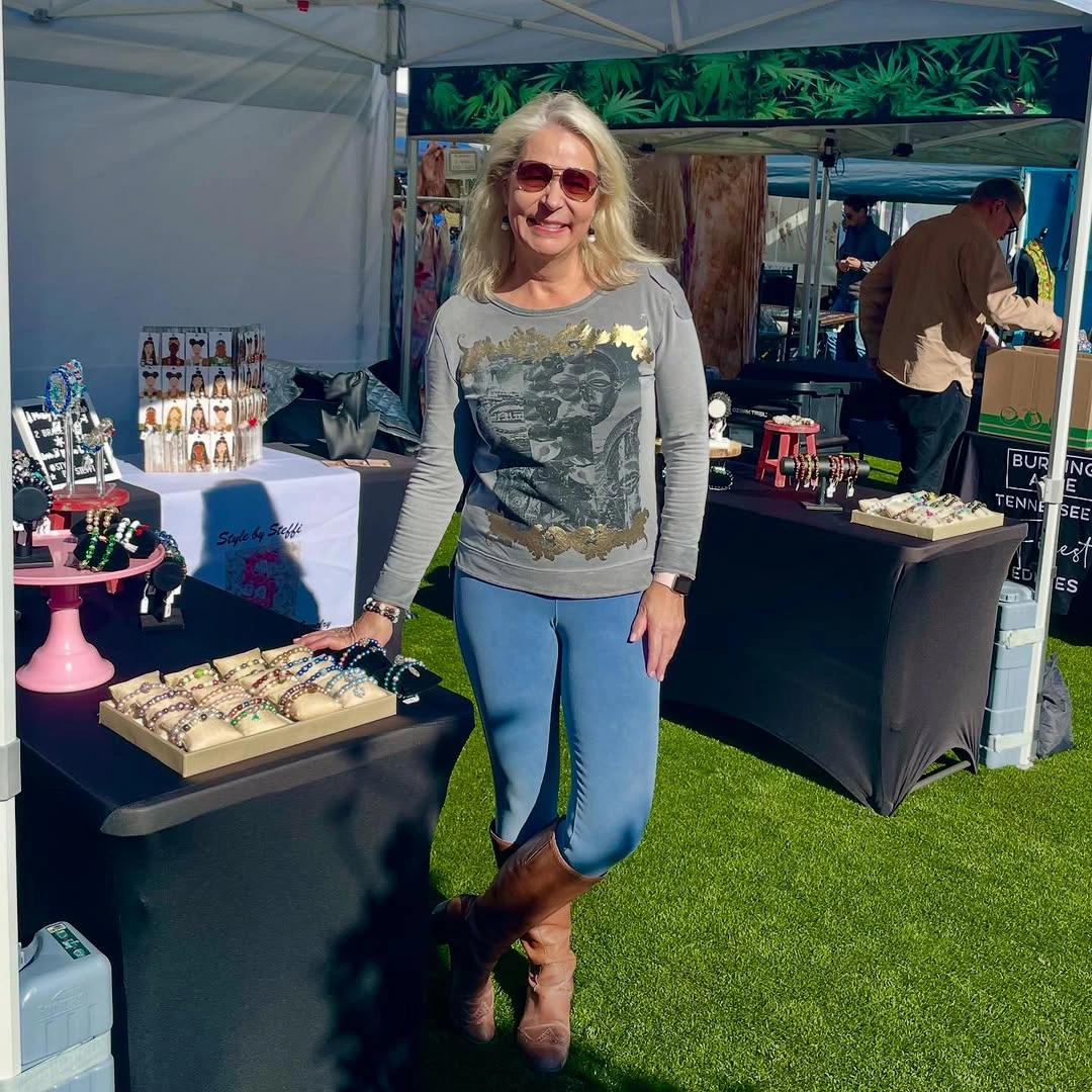 Gray graphic top with blue pants, brown boots and red sunglasses