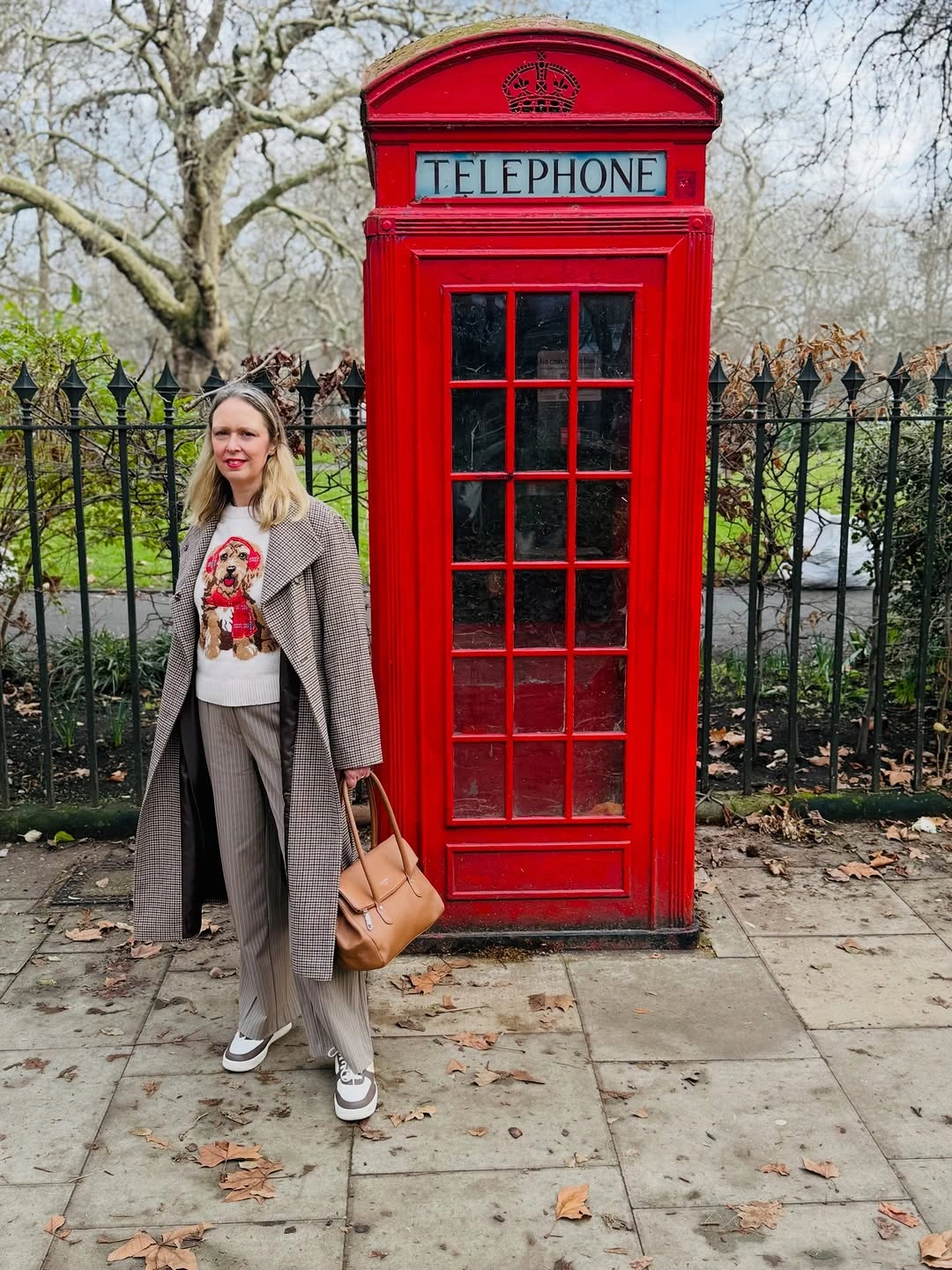 Woman in check coat, graphic top, gray trousers and sneakers