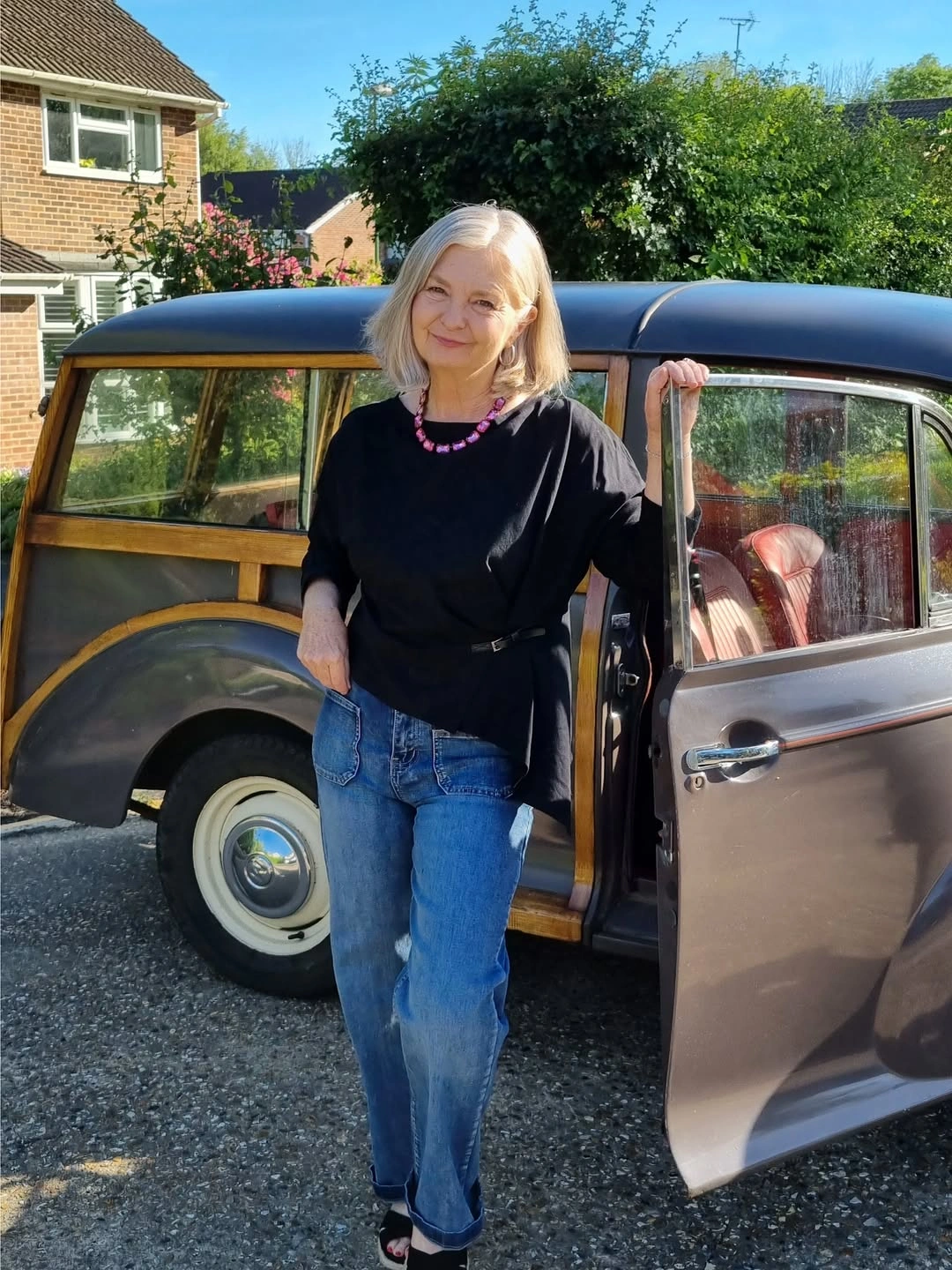 Woman in asymmetrical black top, blue jeans and pink necklace