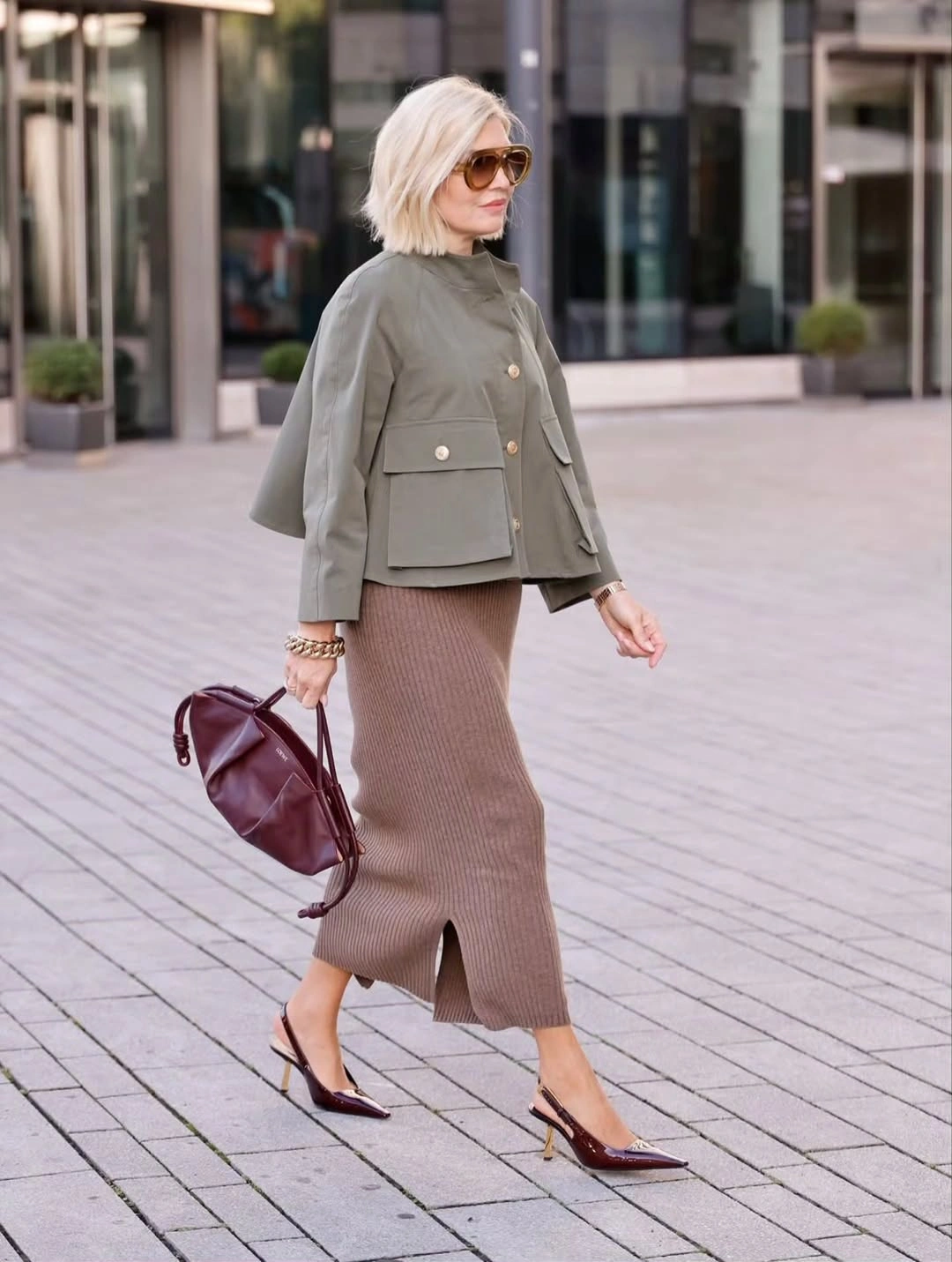 Woman in olive cropped jacket, ribbed skirt and burgundy accessories