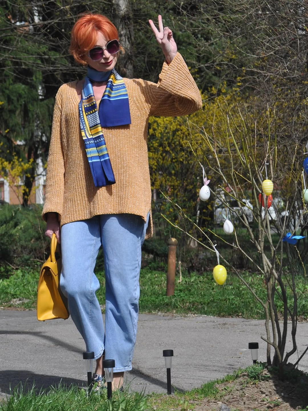 Woman in tan sweater, light jeans and blue yellow scarf