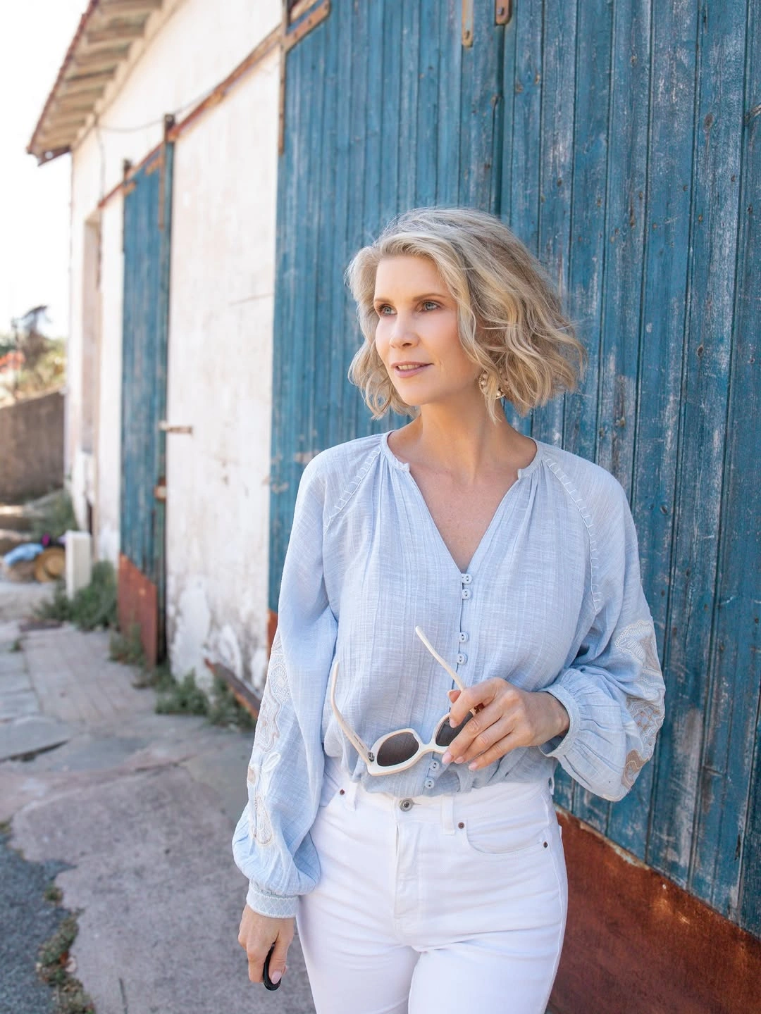 Woman in pale blue blouse, white jeans and white sunglasses