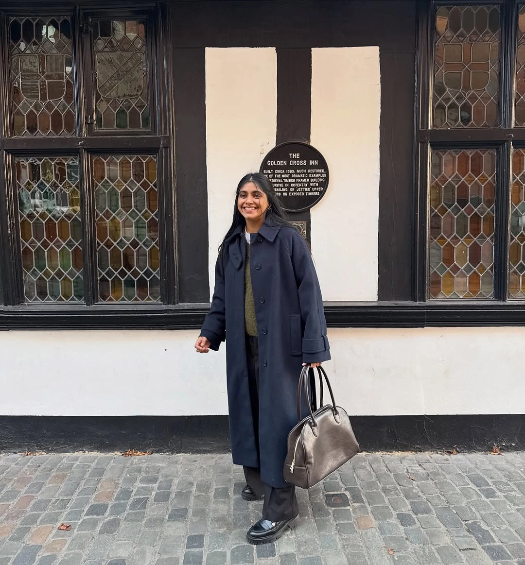 Long navy coat with dark trousers, loafers, and gray tote