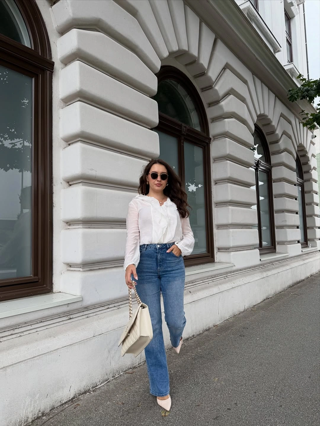 White ruffled blouse with blue jeans, cream pumps, and handbag